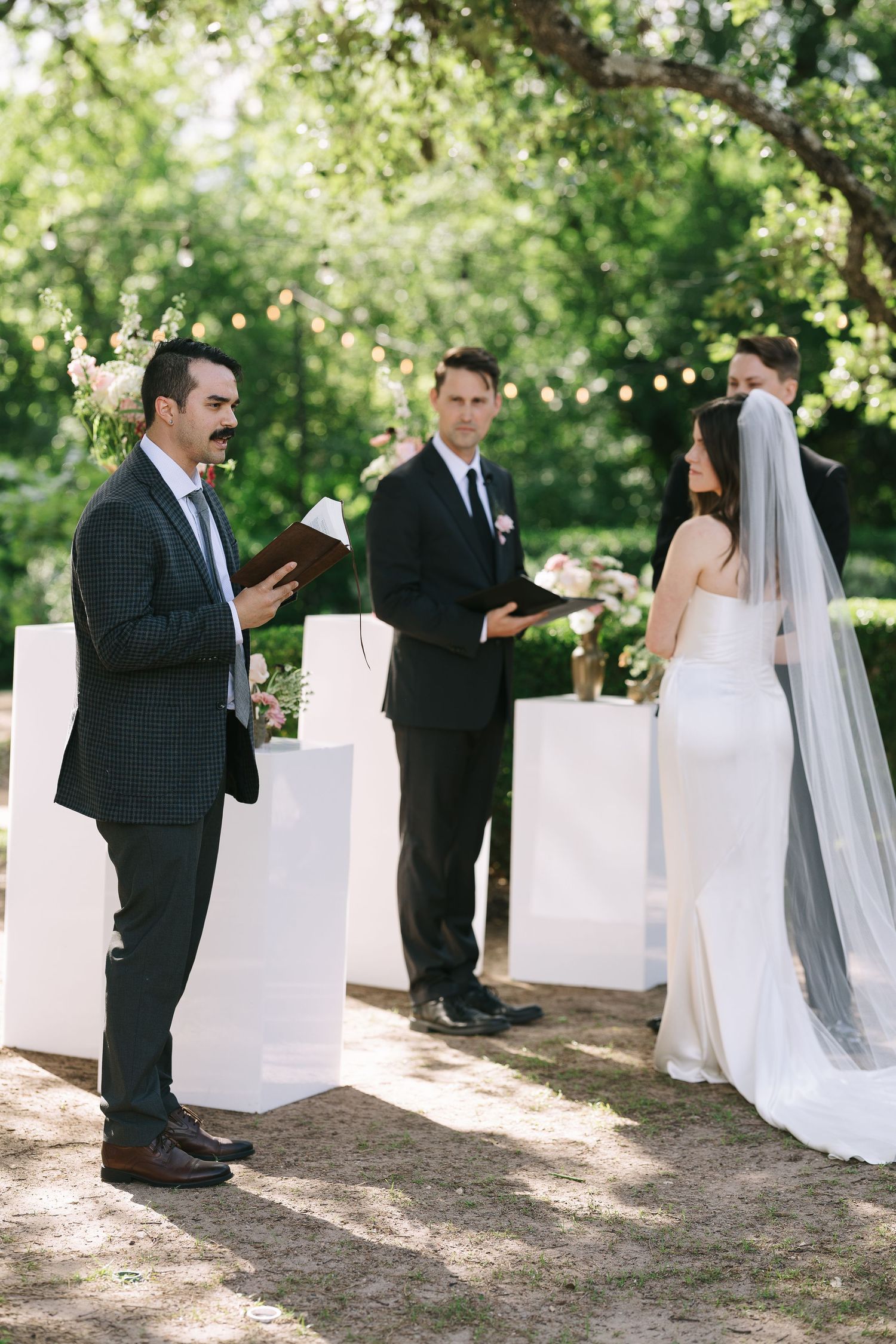 Wedding ceremony setup in a garden with white fabric decorations and natural greenery.