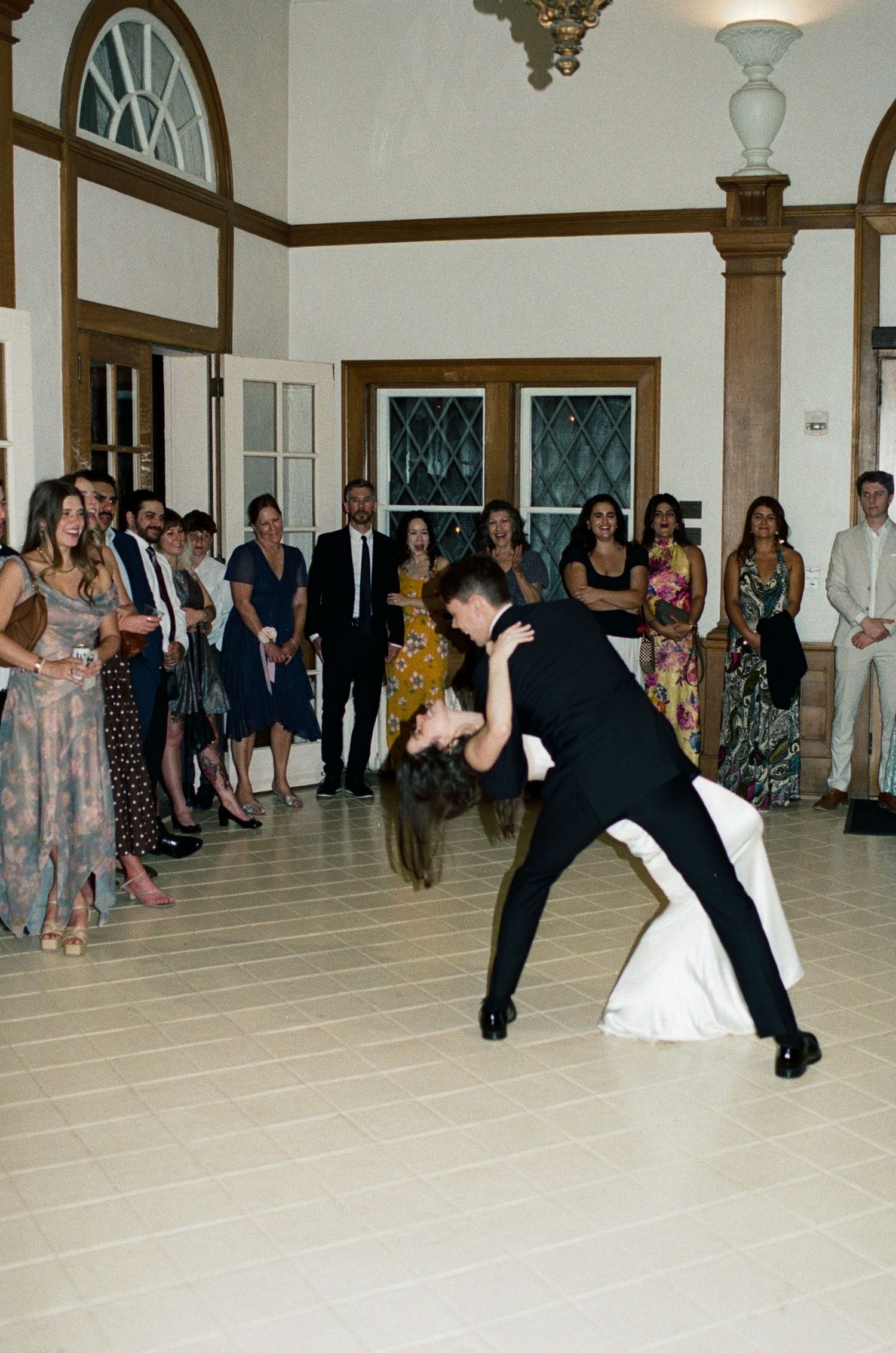 A couple performing a dramatic dance dip on a ballroom floor surrounded by wedding guests.