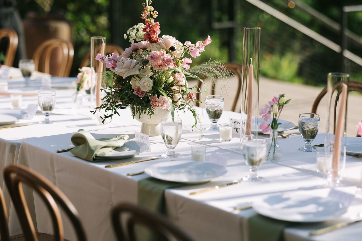 Elegant table settings with floral centerpieces and white linens at an outdoor reception.