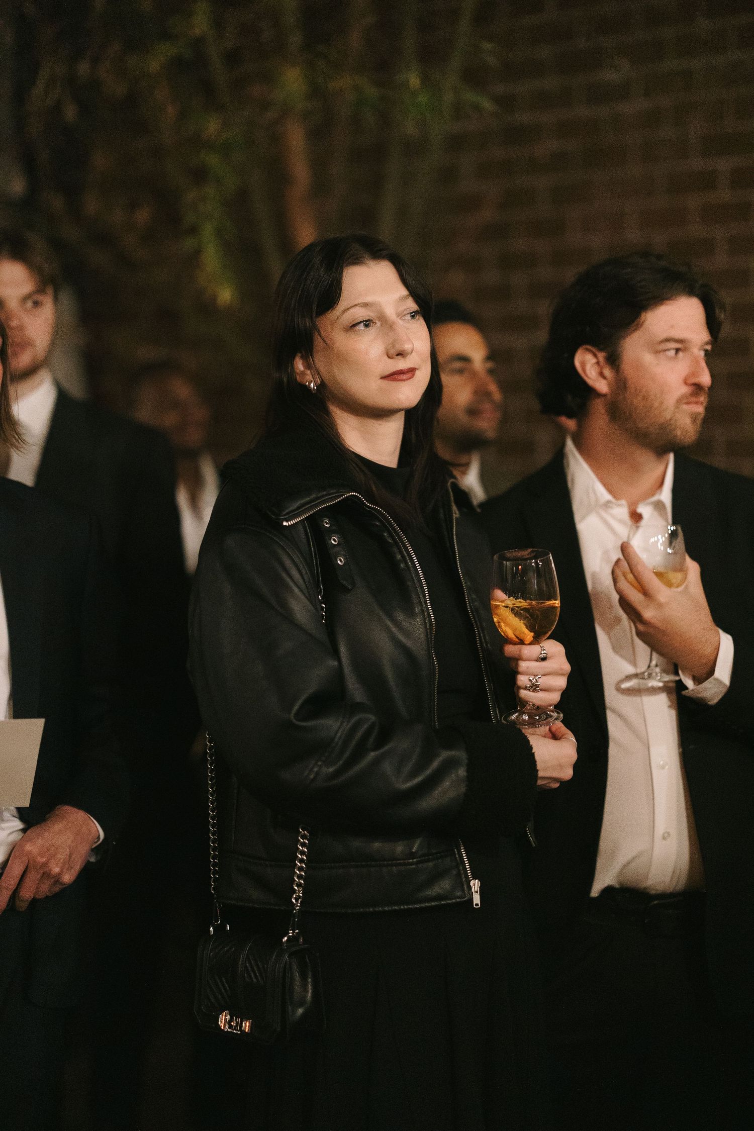 Guests in formal black attire enjoying drinks at an evening wedding reception.