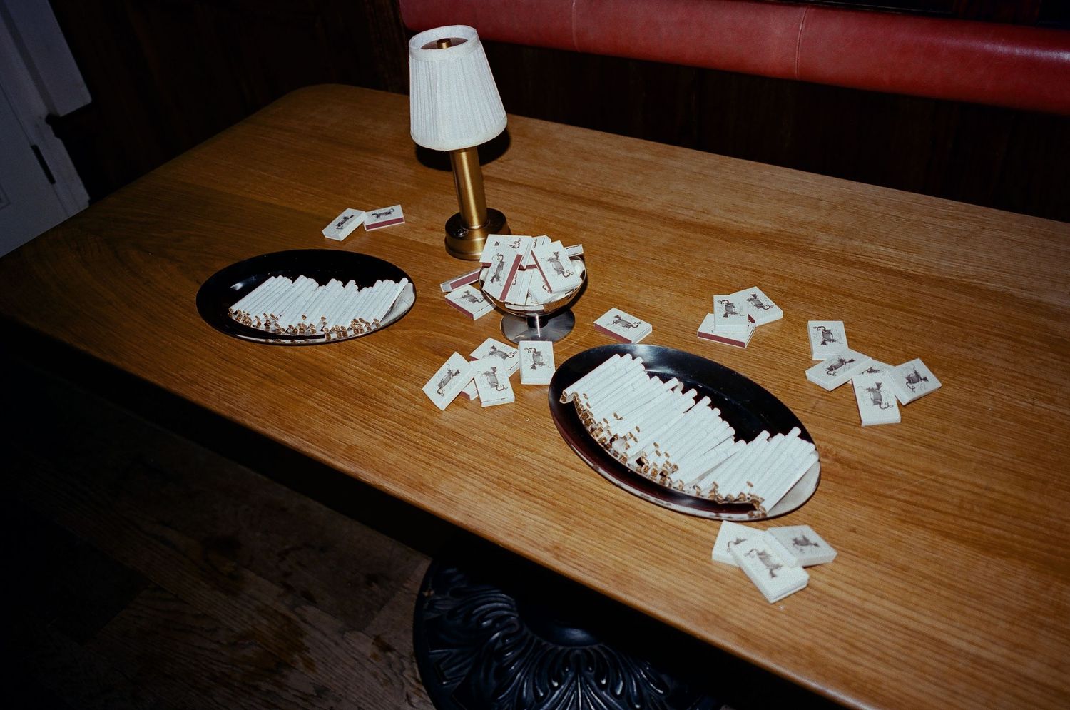 Playing cards and two black plates scattered on a wooden table with a small white table lamp.