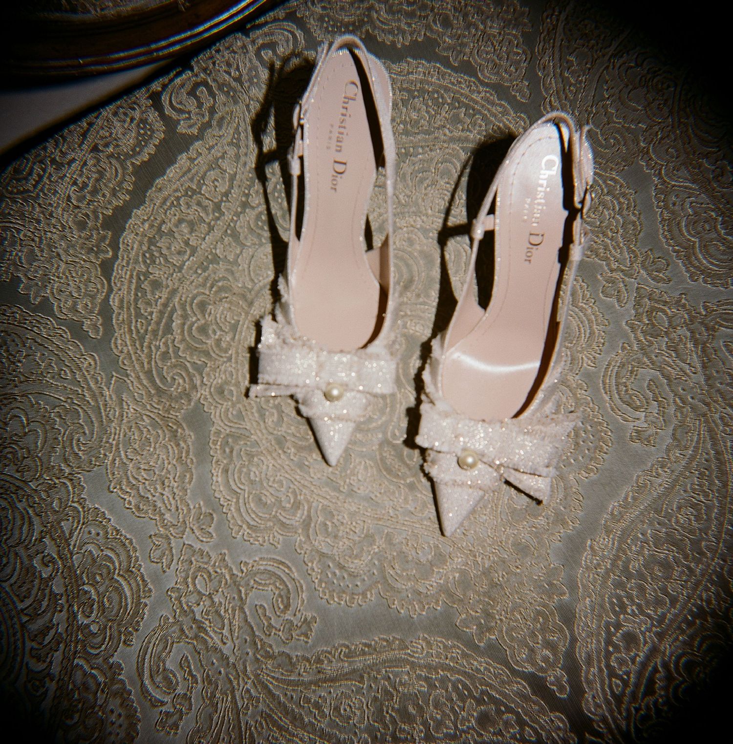 Elegant nude patent leather stiletto heels displayed on a delicate lace fabric background.
