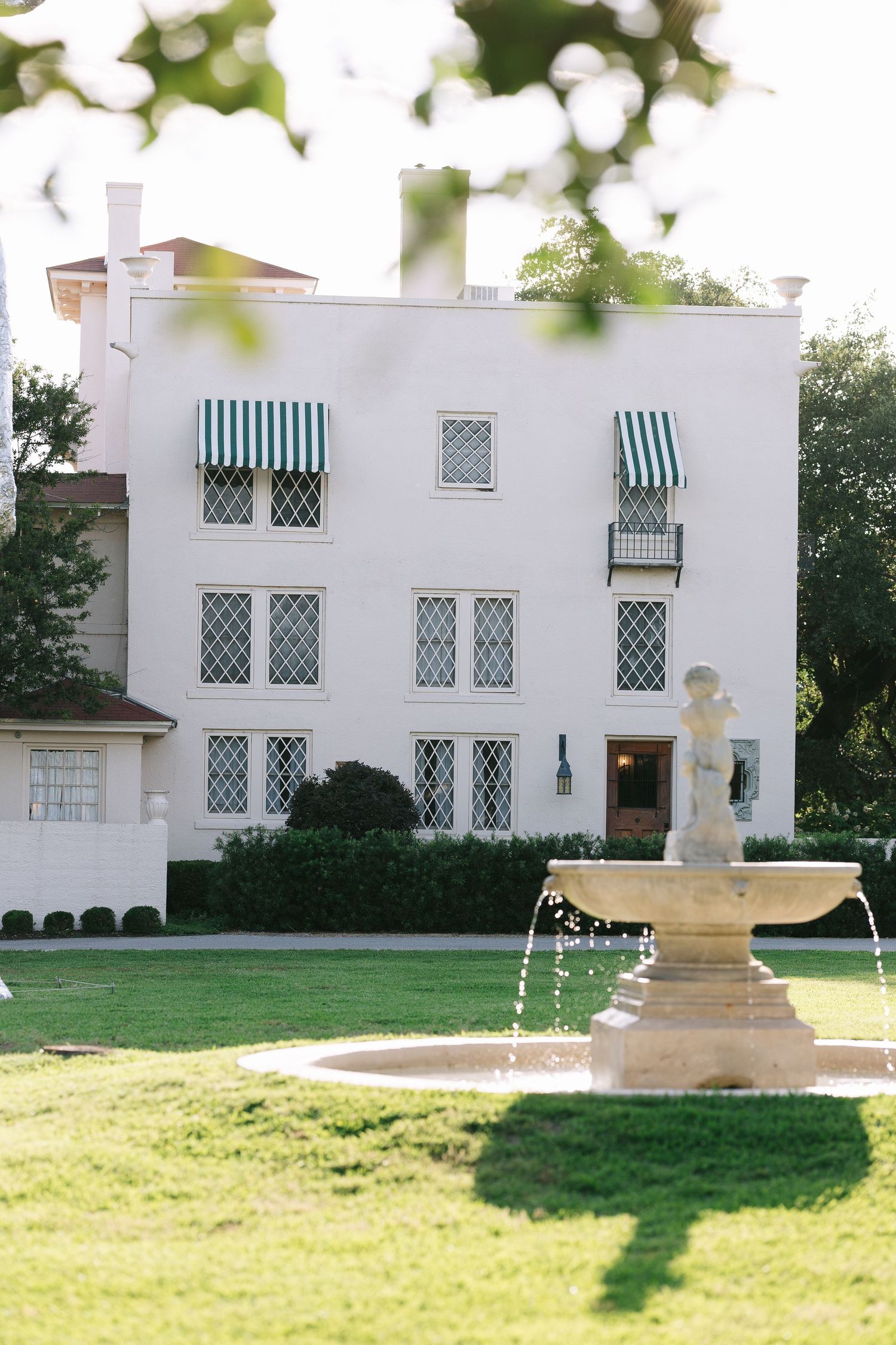 White mansion with green striped awnings and manicured lawn features classical architecture.