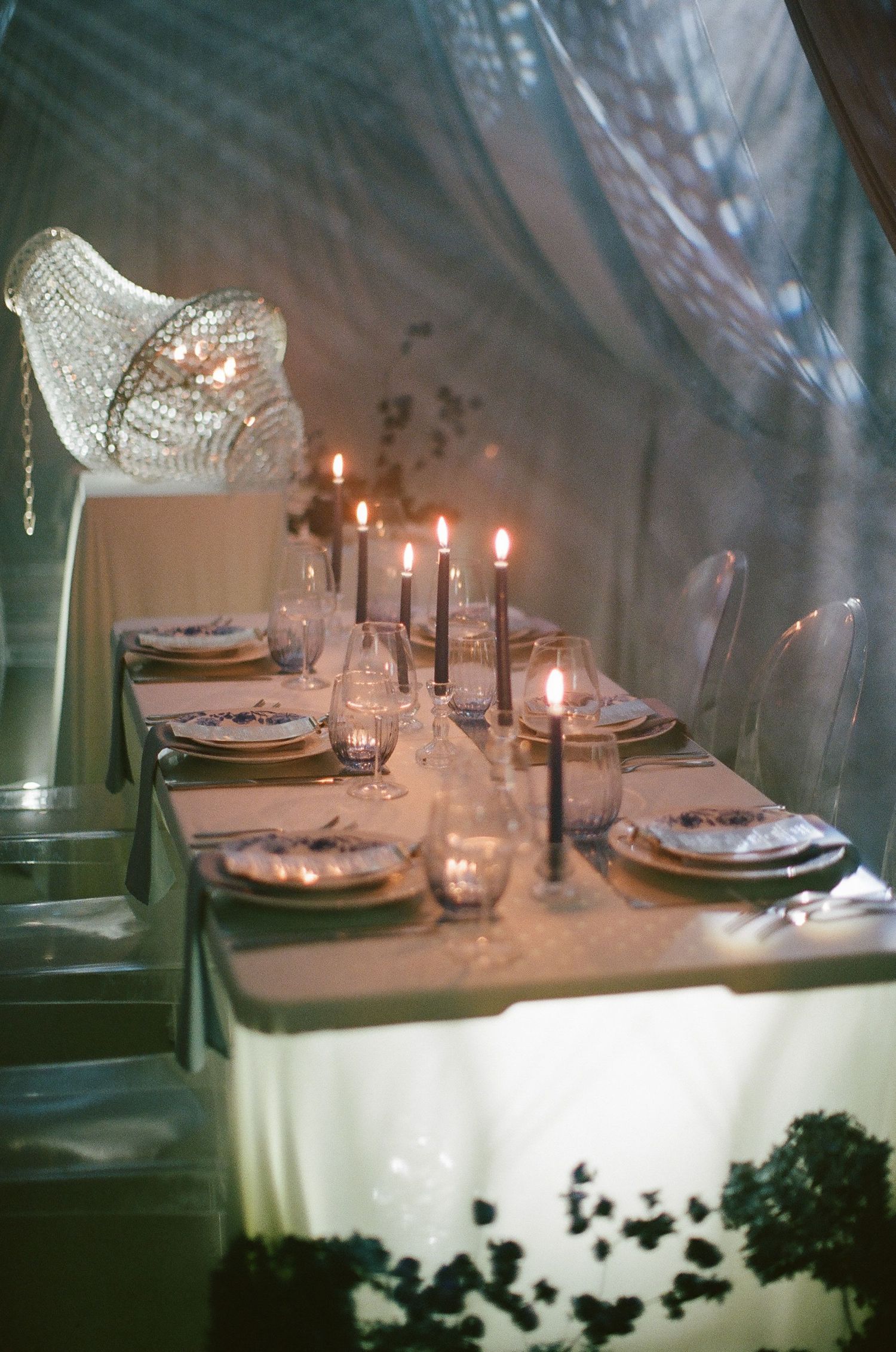Elegant candlelit dinner table with black taper candles, crystal chandelier, and formal place settings under a draped tent.