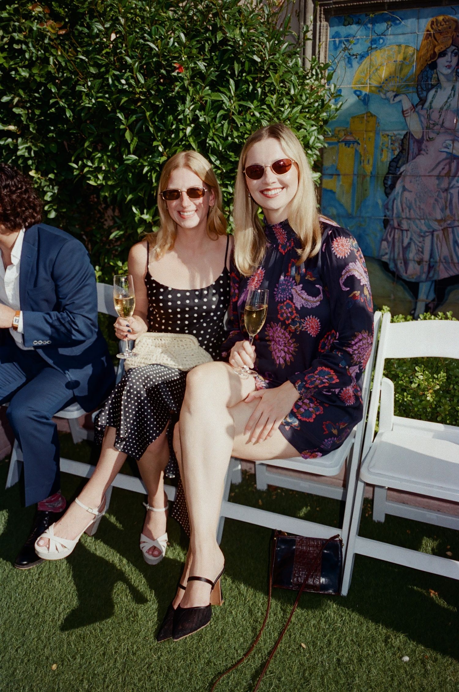 Two people sit together on a white bench in an outdoor garden setting.