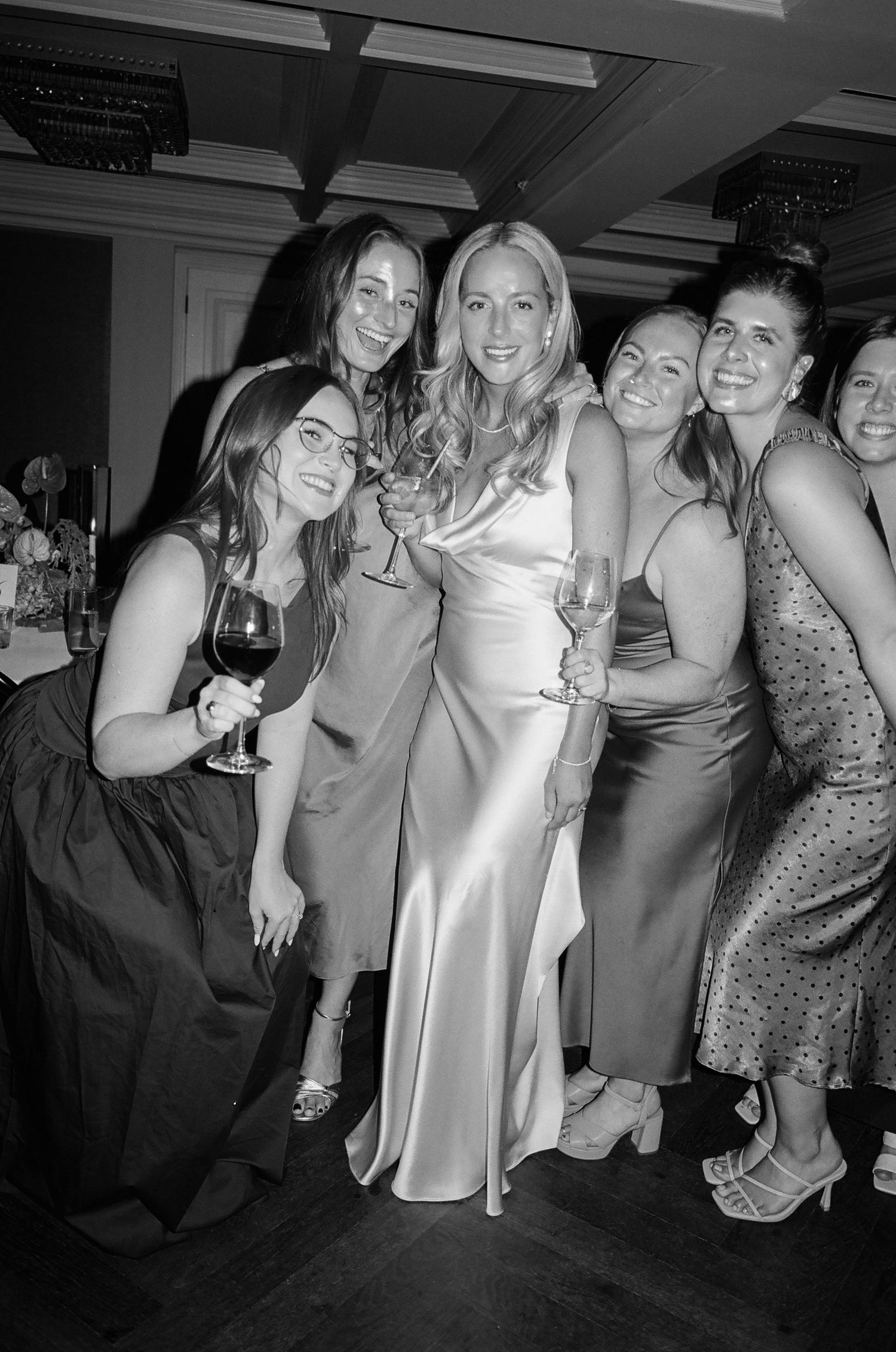 A group of friends in formal attire laugh and pose together at a party celebration.