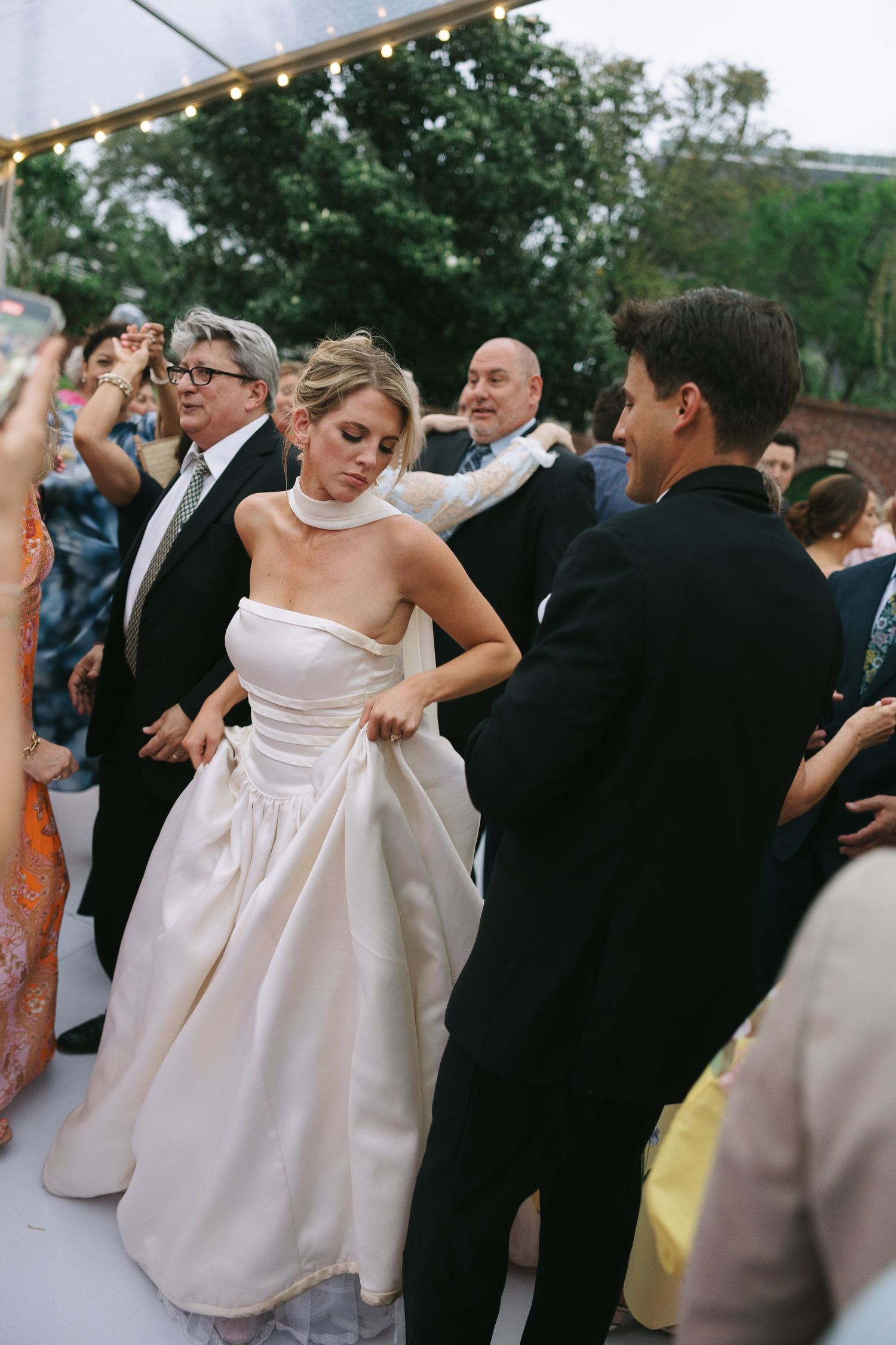 Guests in formal attire dance together at an elegant outdoor wedding reception.