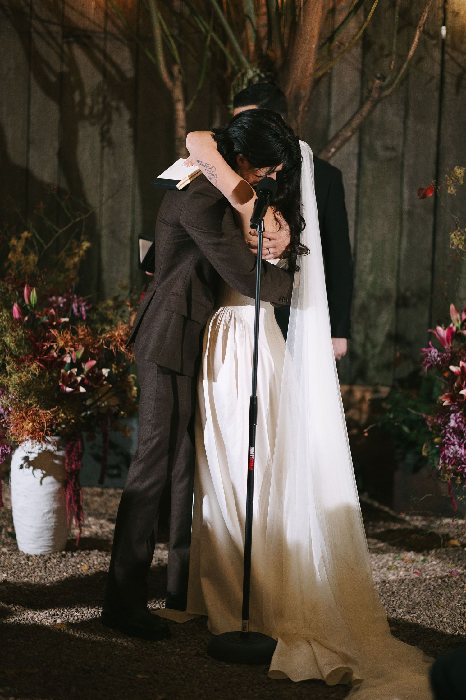 A tender embrace between newlyweds in an outdoor garden setting with soft evening lighting.
