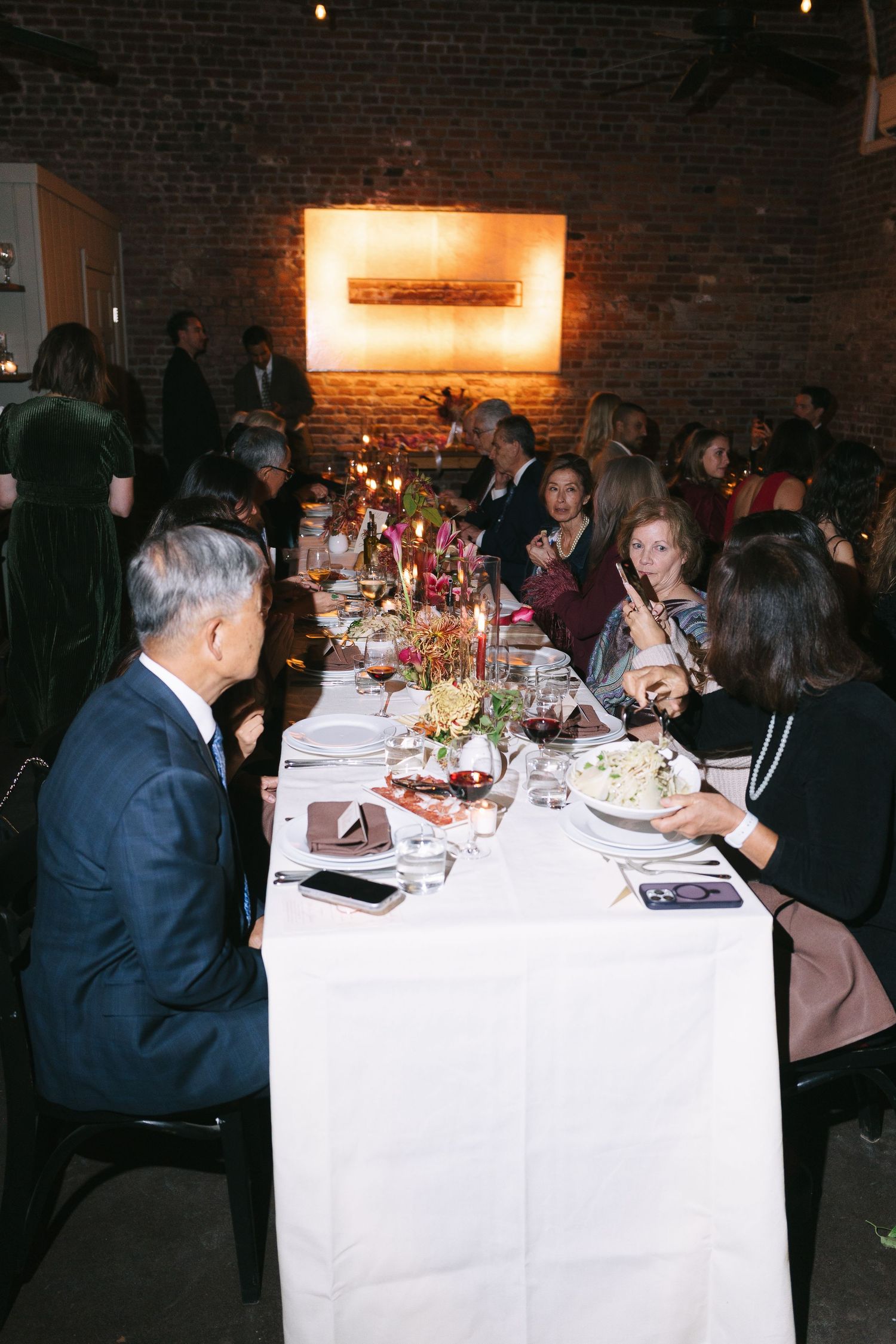 Guests dining at elegant tables with white tablecloths in a brick-walled venue.