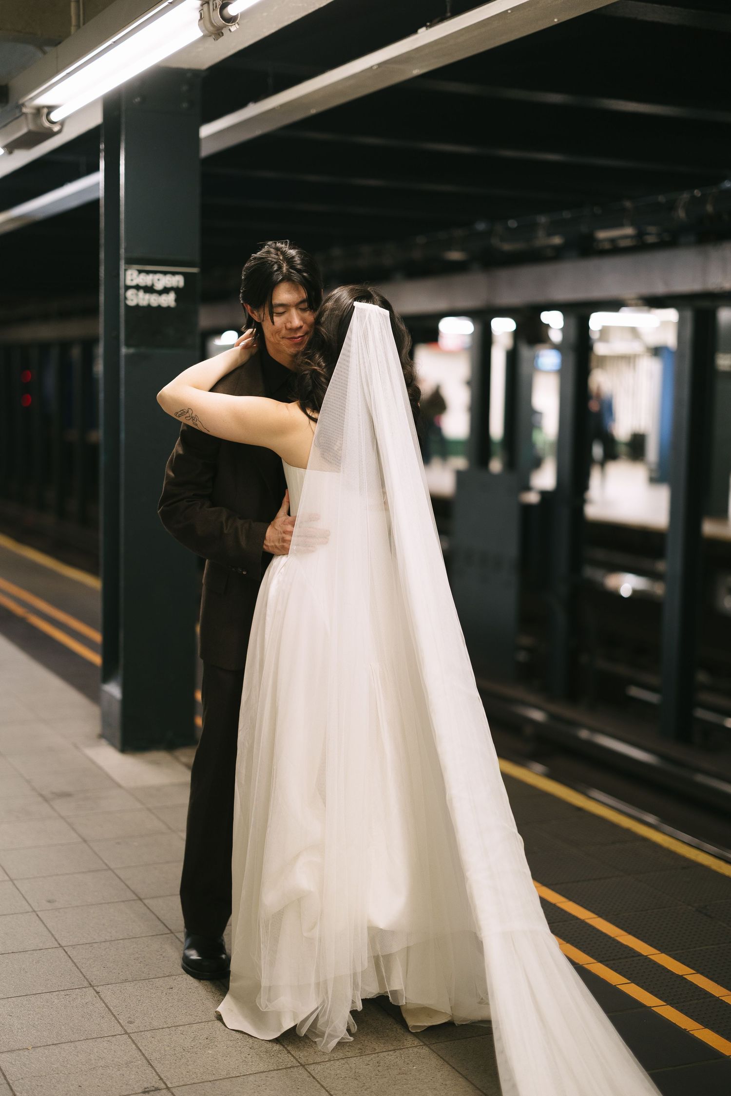 Happy couple embracing on subway platform with bride's flowing white dress and veil.