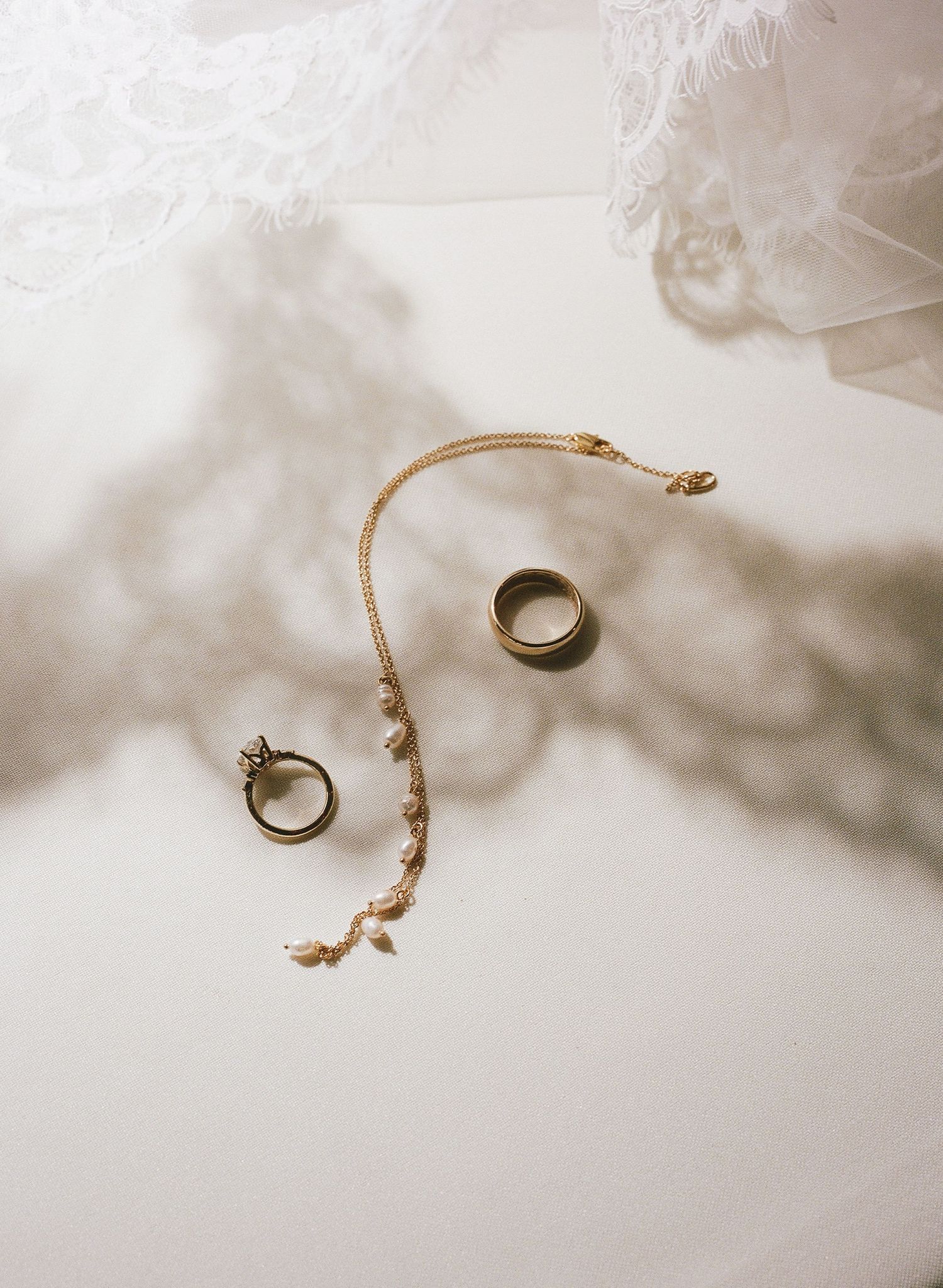 Gold wedding rings and jewelry arranged on white fabric in a minimalist style.