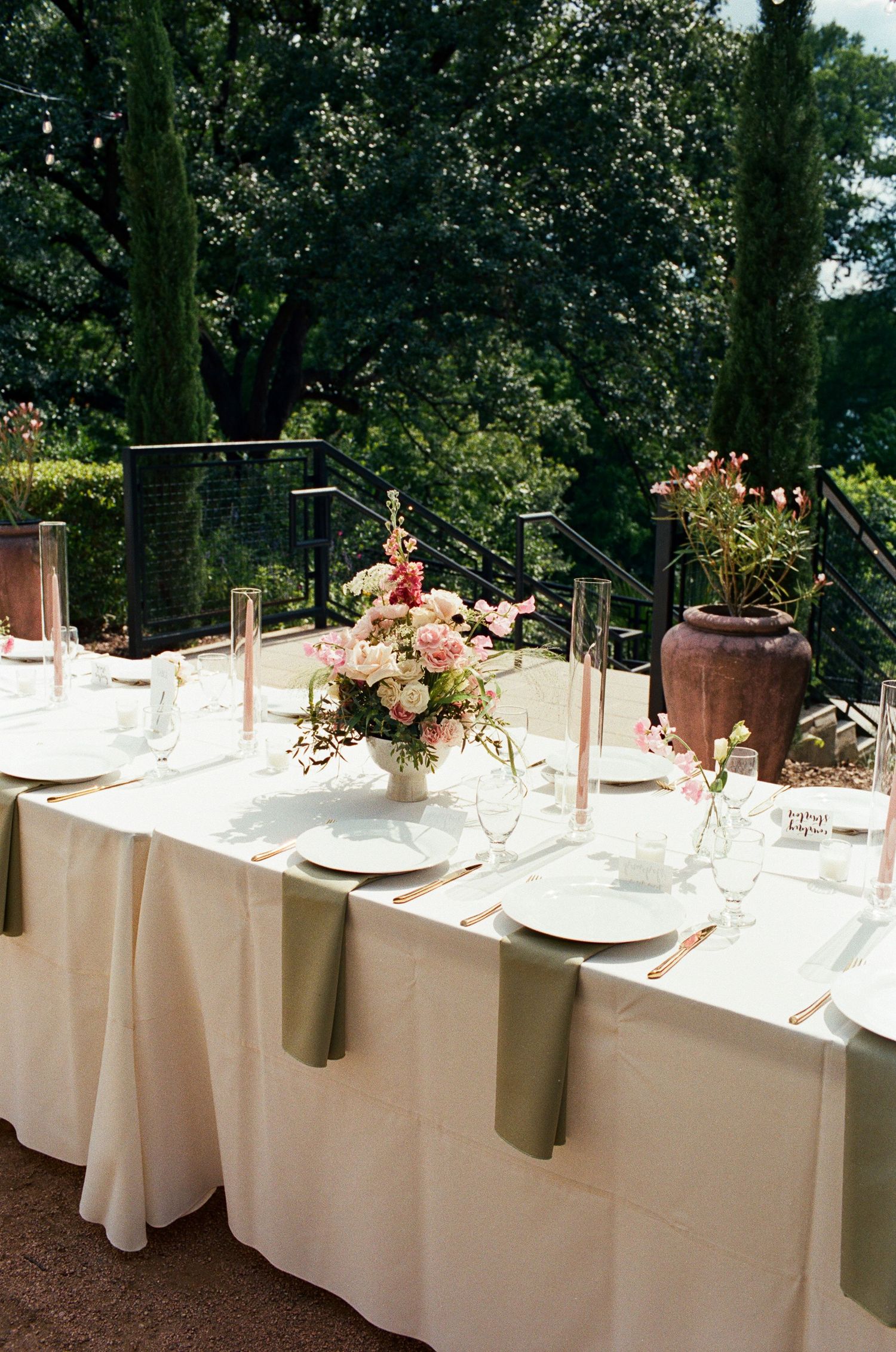 Long white dining tables decorated with floral centerpieces and place settings in an outdoor setting.