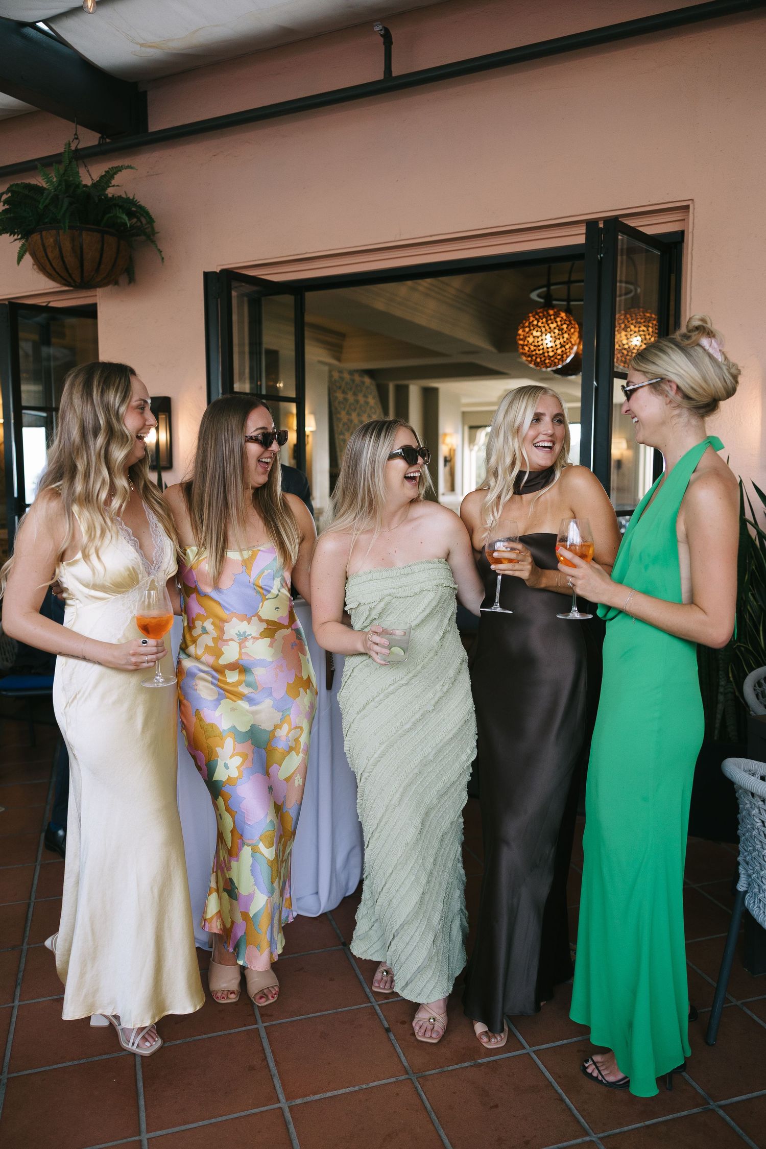 Wedding guests in colorful summer dresses mingling at an indoor venue.