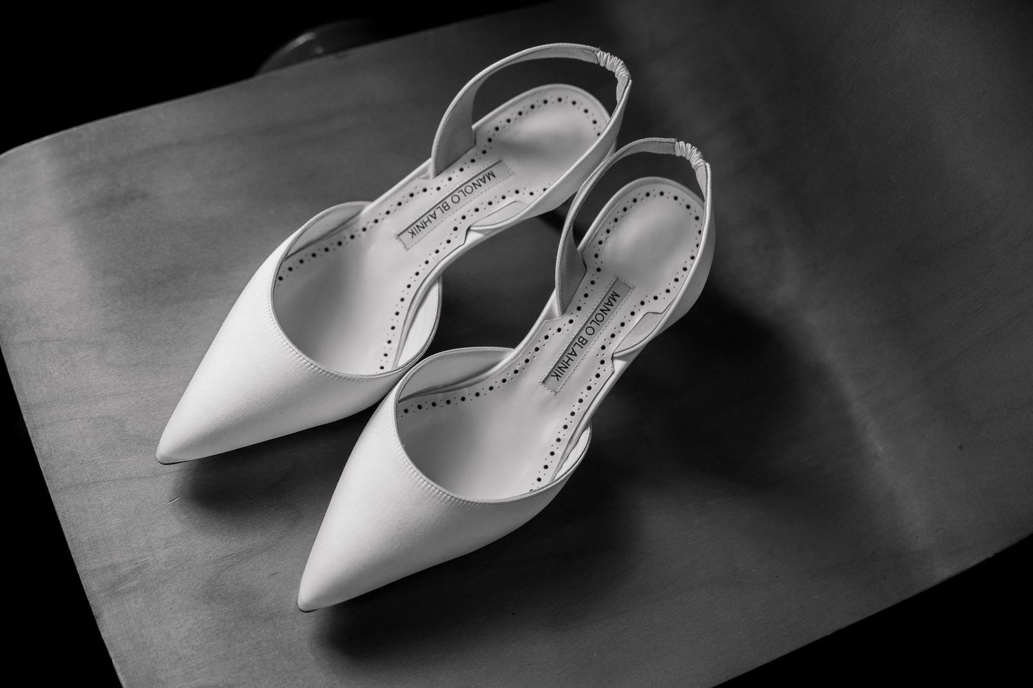 Elegant white bridal shoes photographed in dramatic black and white lighting.