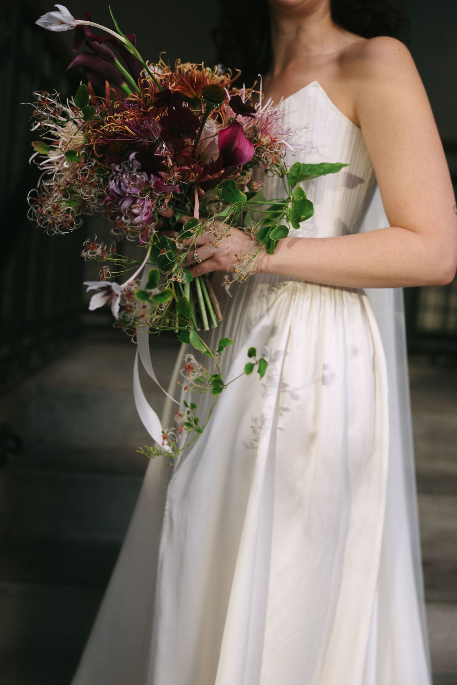 Close-up of a white wedding dress with a vibrant burgundy and purple floral bouquet.