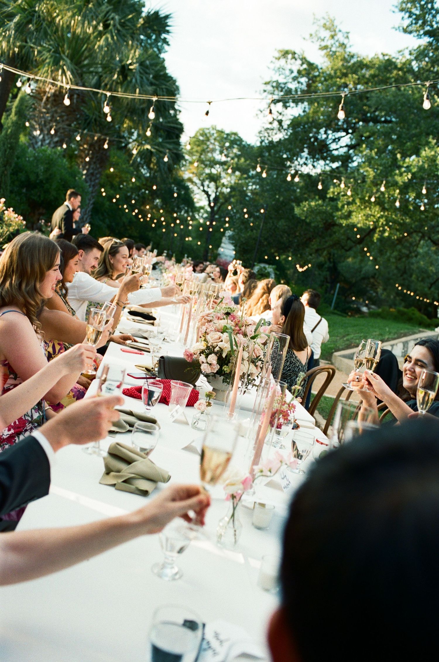 Outdoor wedding reception dinner table with string lights and glassware at dusk.