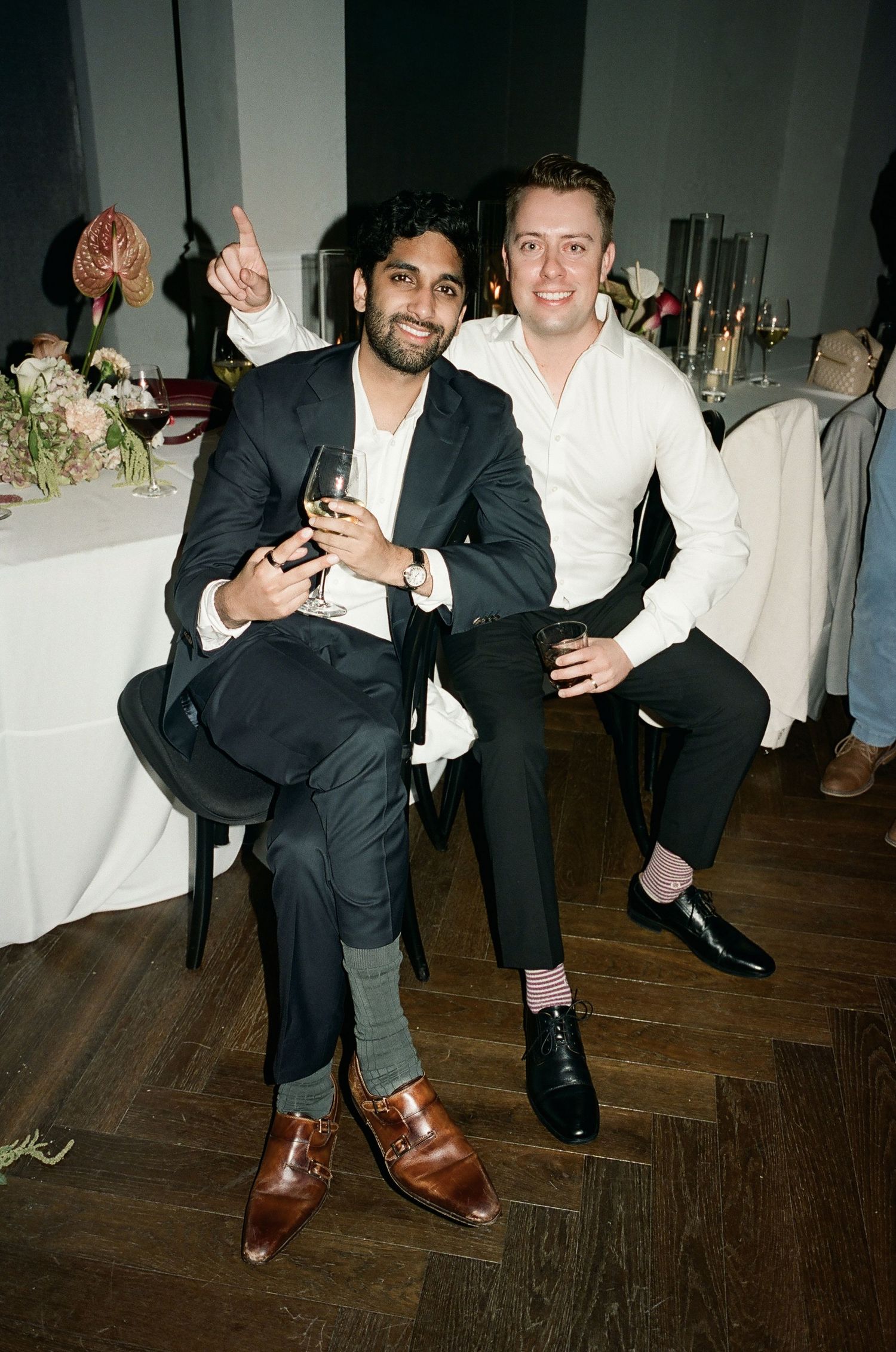 Two guests in formal attire pose together at a wedding reception with drinks.