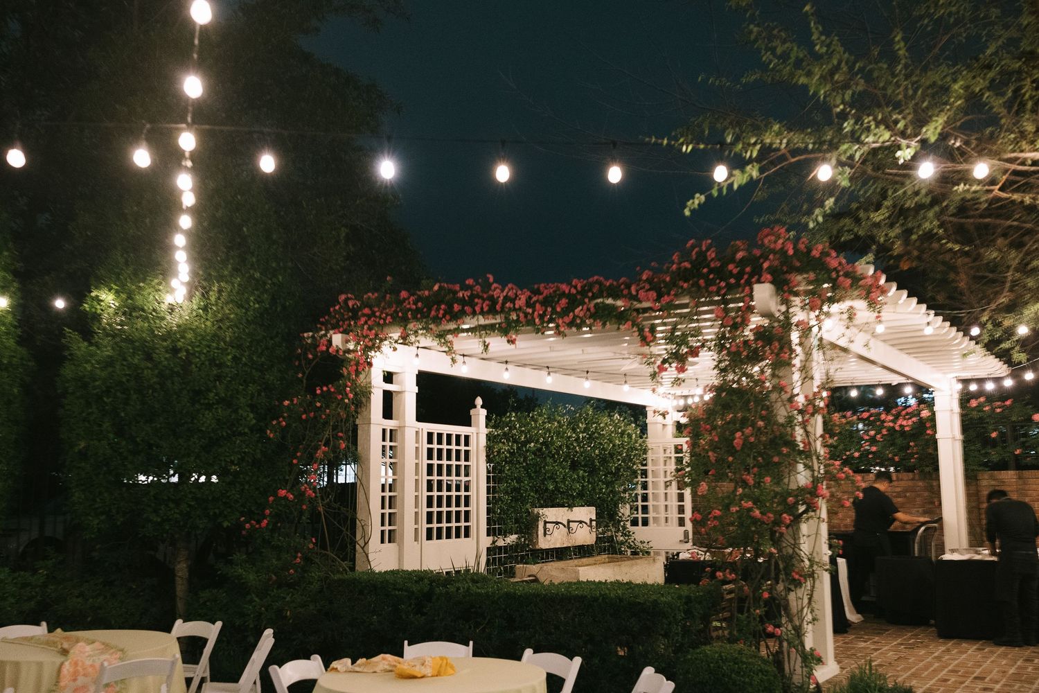 Outdoor wedding venue with string lights and white pergola at night.