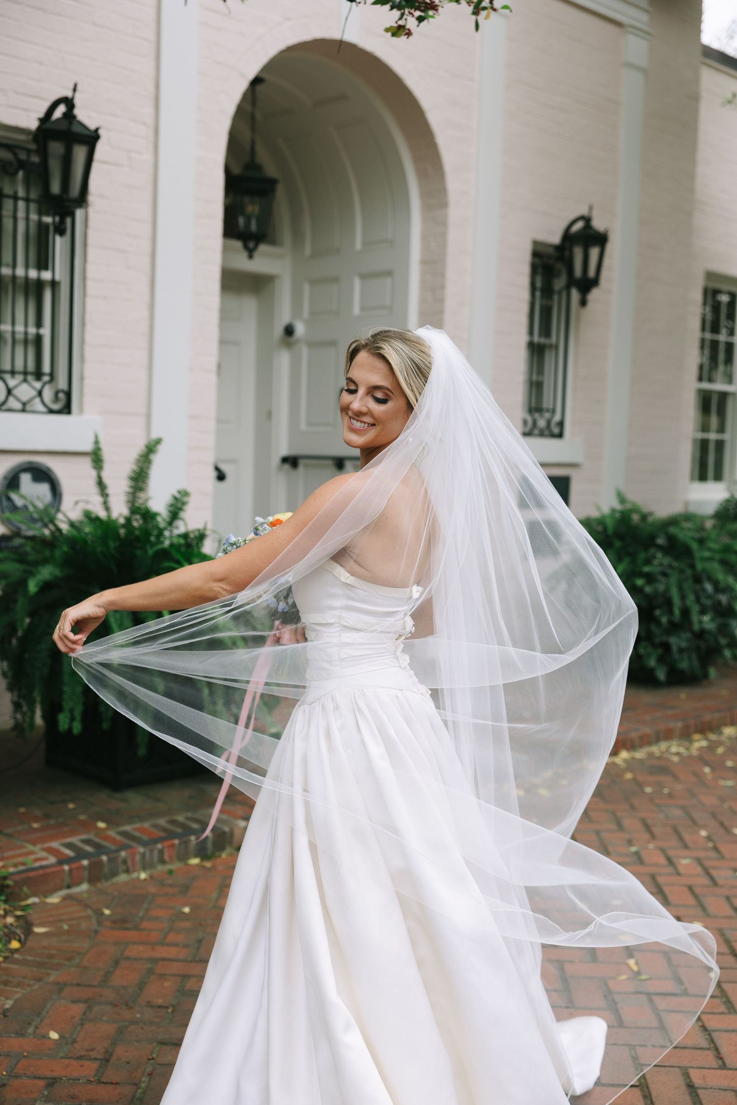 Bride in flowing white dress twirls gracefully on brick pathway.