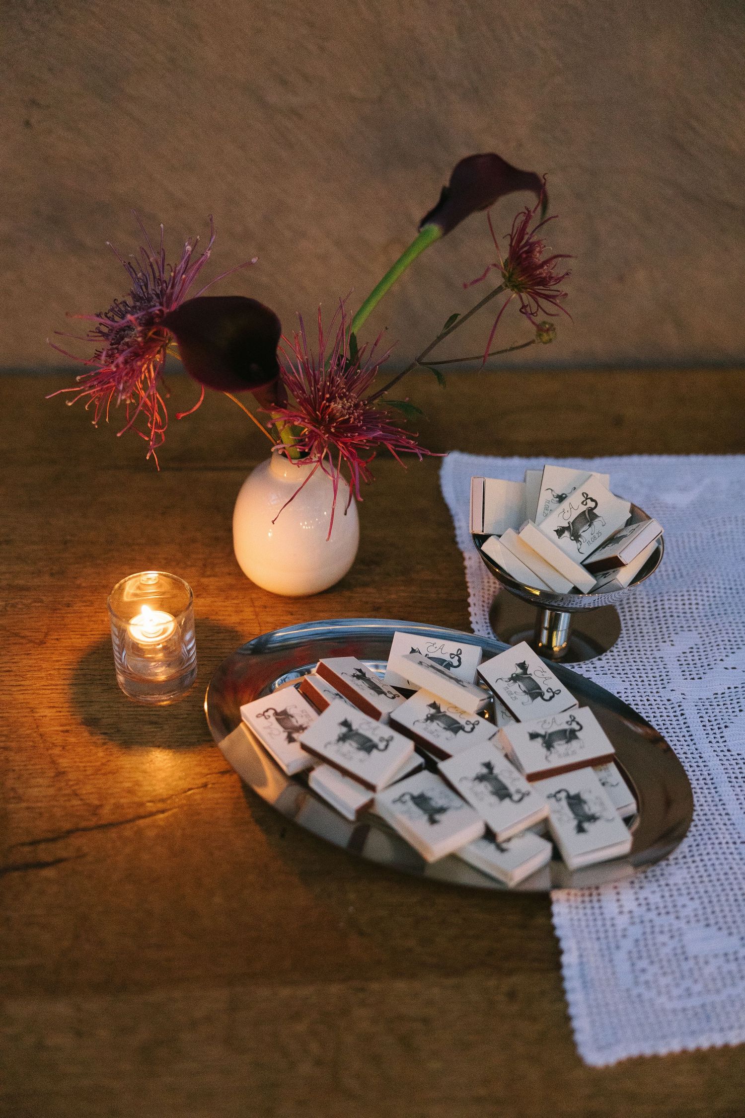 Place cards and wedding favors displayed on rustic wooden table with candlelight and floral decorations.