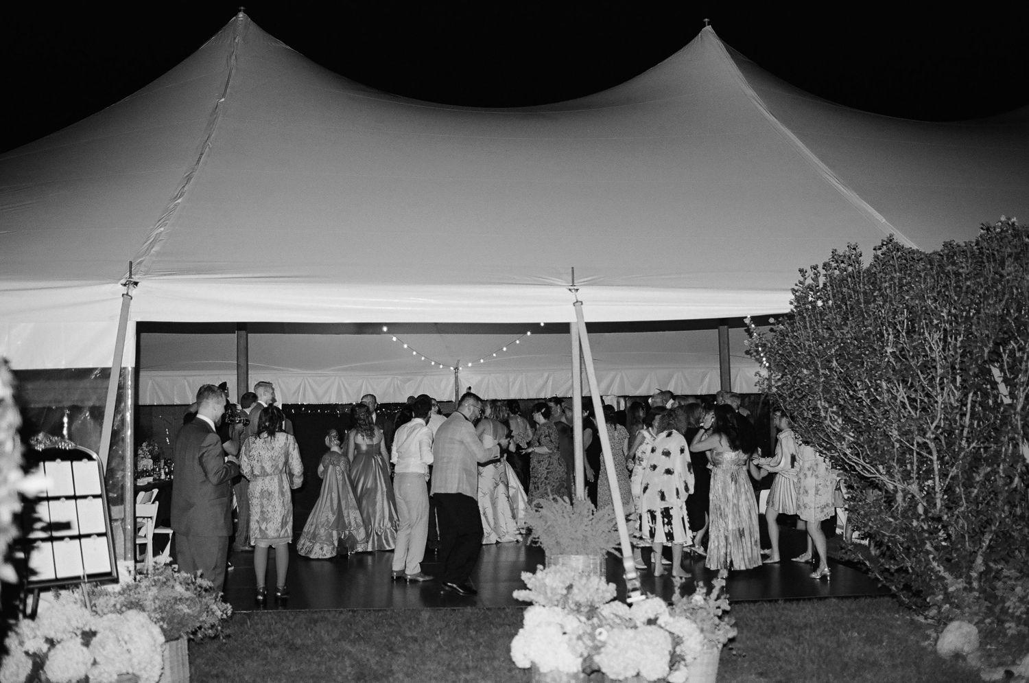 An outdoor wedding reception under white tents with guests mingling at dusk.