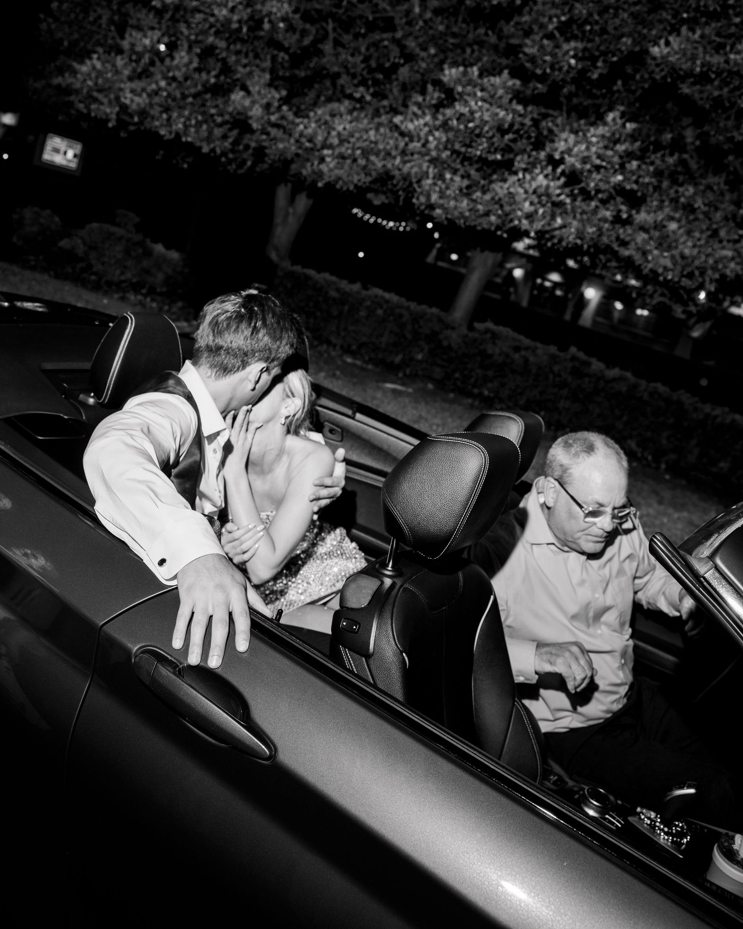 Black and white photo of people sitting in a convertible car at night.