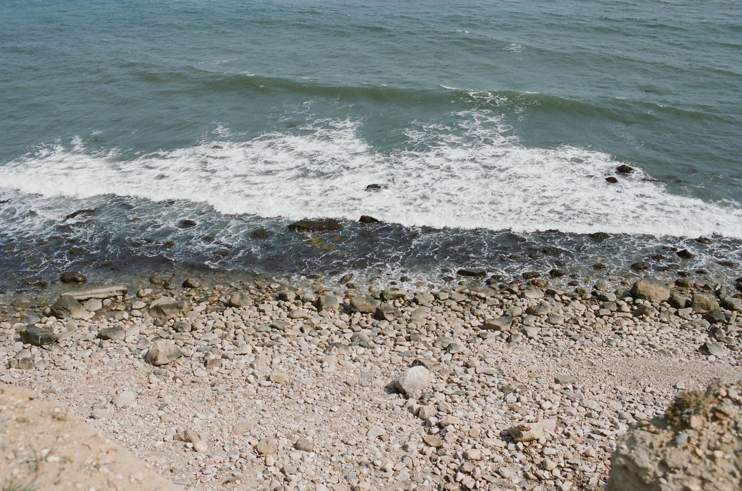 Ocean waves crash against a rocky coastline on a sunny day.