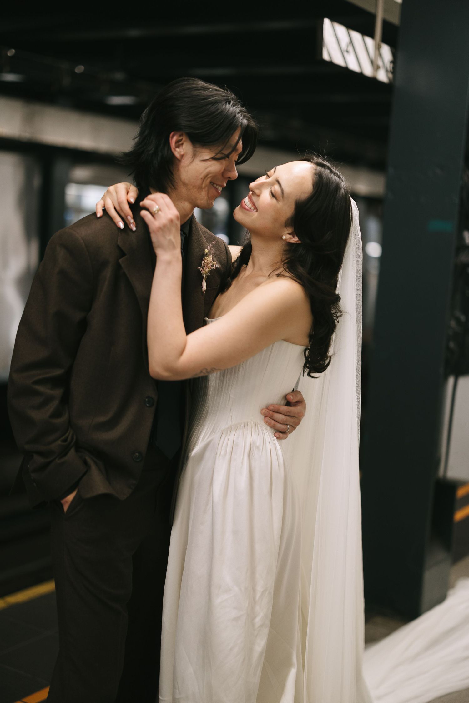 Joyful wedding couple laughs together in dimly lit indoor setting.