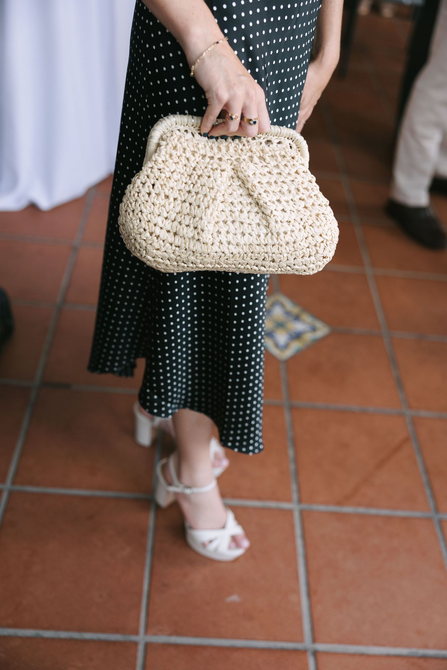 Person holding a cream-colored crochet clutch purse against polka dot dress.