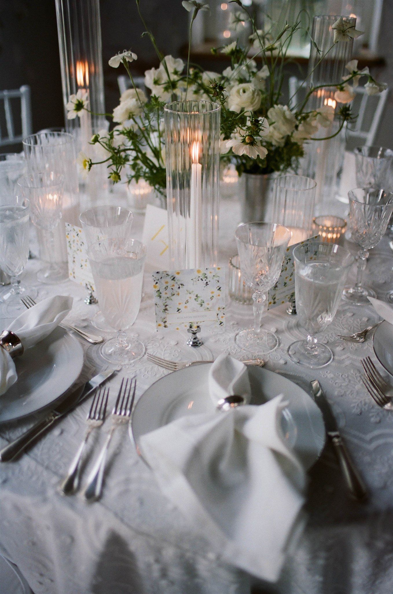 Elegant white wedding reception table with crystal glasses and floral centerpieces.
