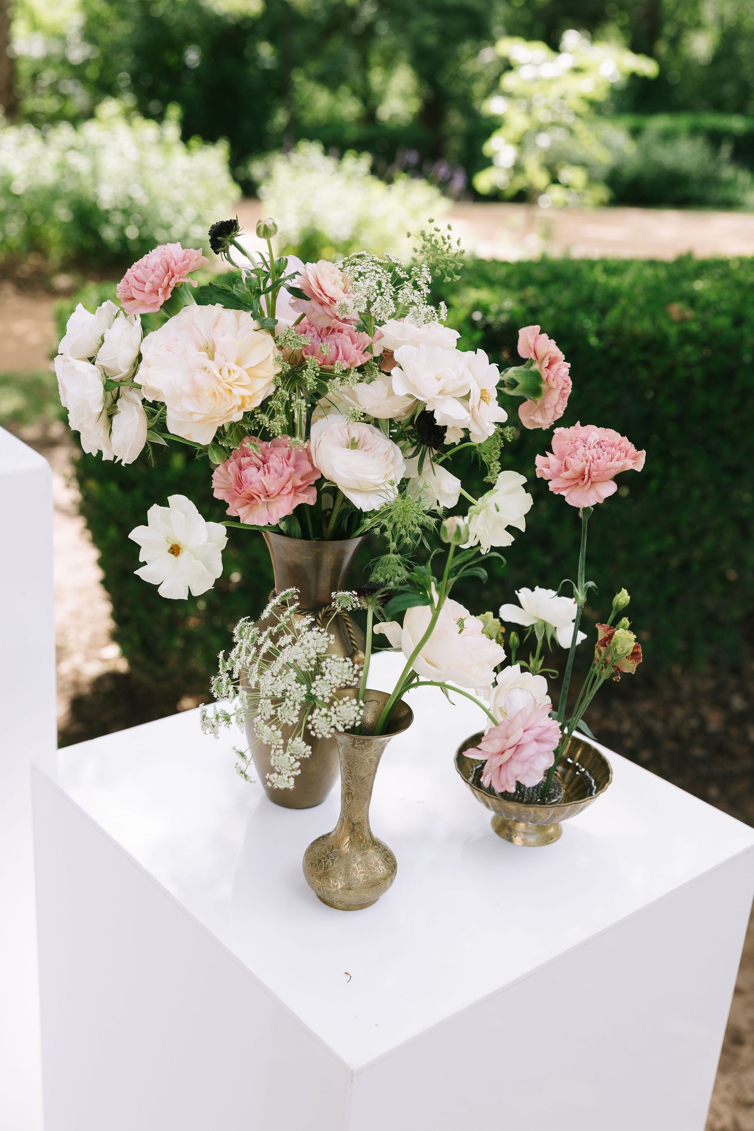 Pink and white floral arrangements in gold vases displayed on white pedestal.