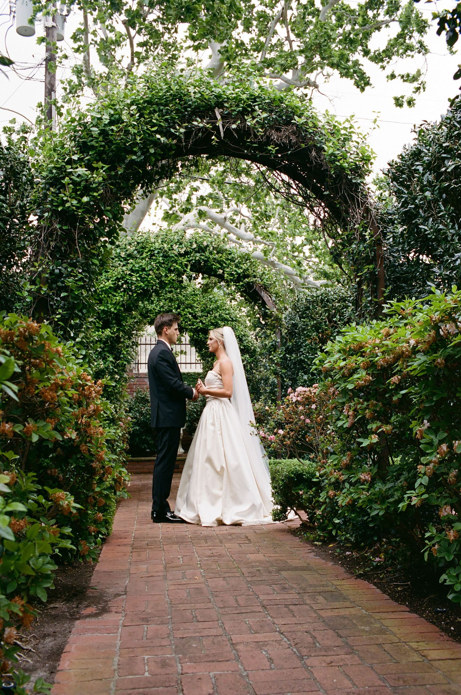 Romantic garden wedding portraits along a brick pathway surrounded by greenery.