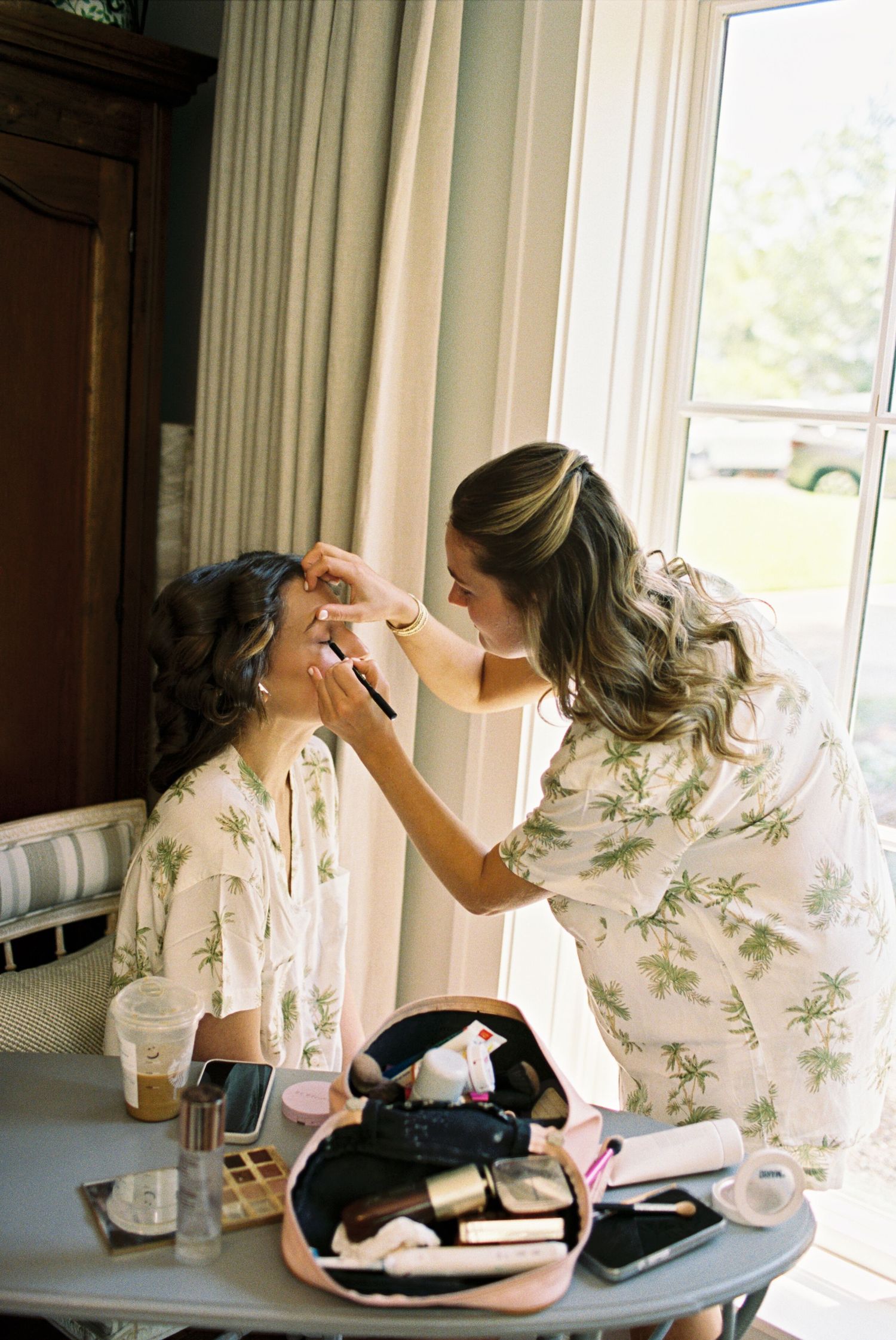 Wedding preparation scene with makeup application in a sunlit room.
