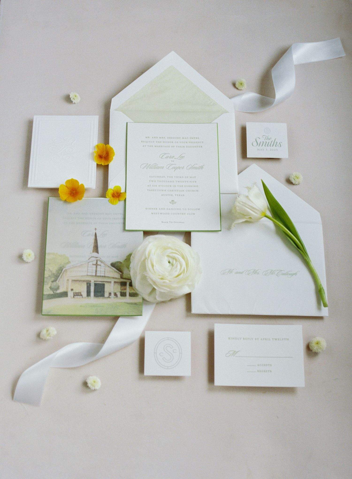 Elegant wedding invitation suite with white flowers and delicate stationery laid out on a light gray background.