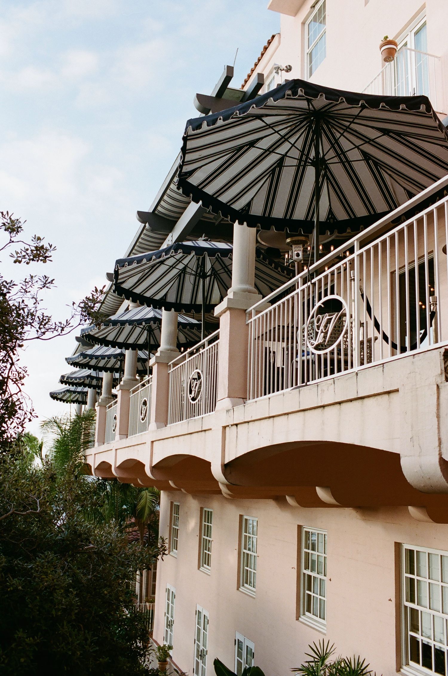Black parasol awnings line the balcony of a pink Mediterranean-style building.