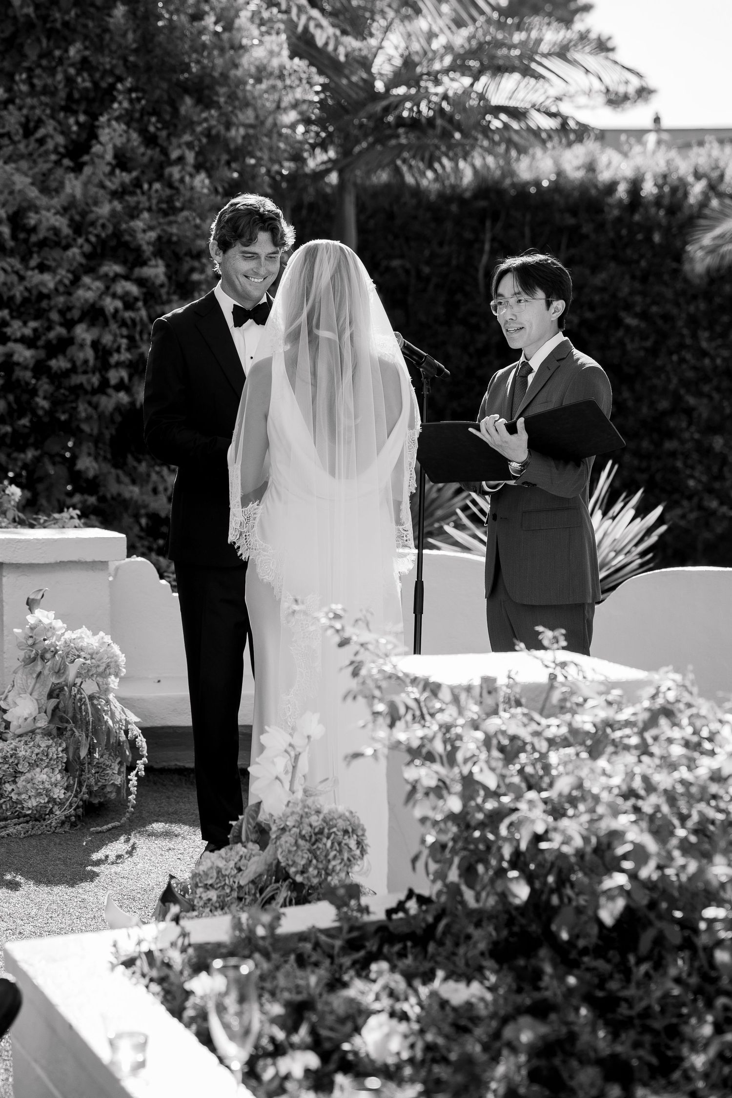 Black and white wedding ceremony photo with floral arrangements in the foreground.
