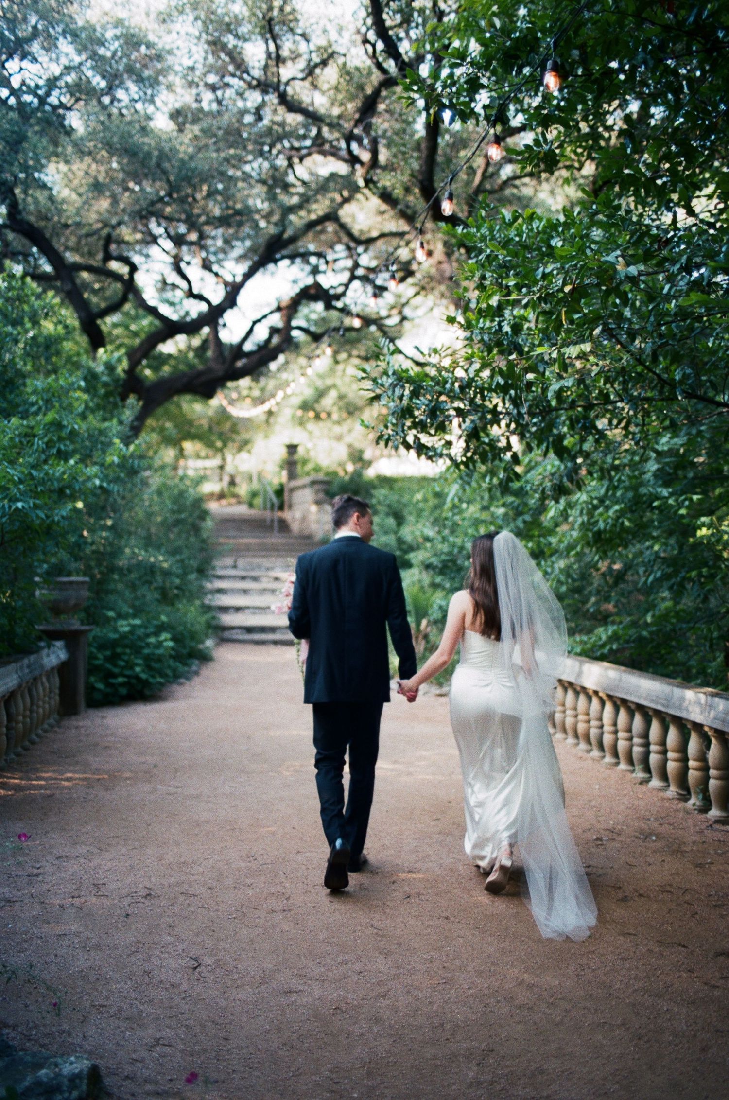 A couple walks hand in hand down a tree-lined path after their wedding ceremony.