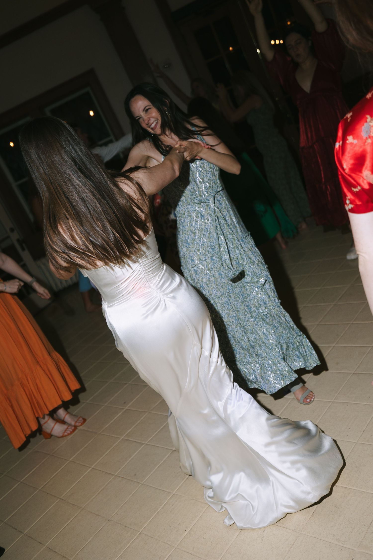 Wedding guests dancing, with someone in a white bridal gown visible on the dance floor.