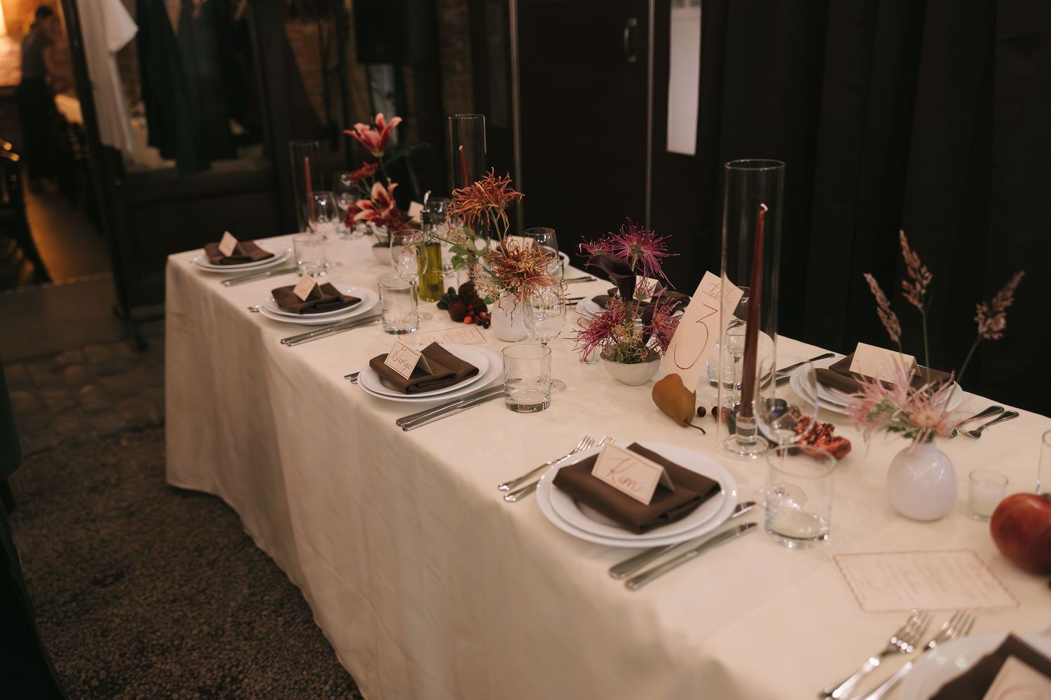 Elegant table setting with white linens, dark napkins, and floral centerpieces in a dimly lit room.