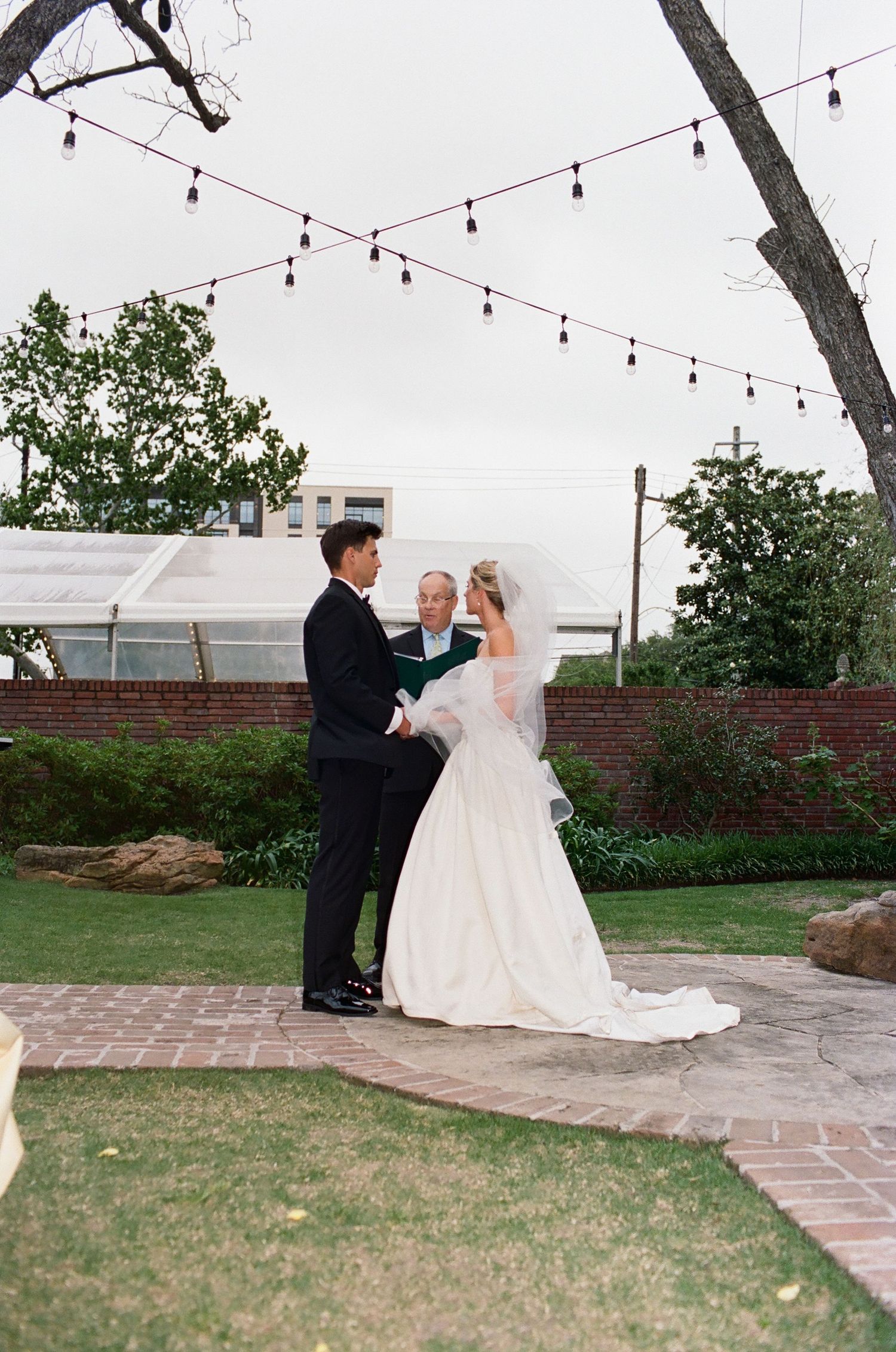 An outdoor wedding ceremony with string lights and brick pathways in a garden setting.