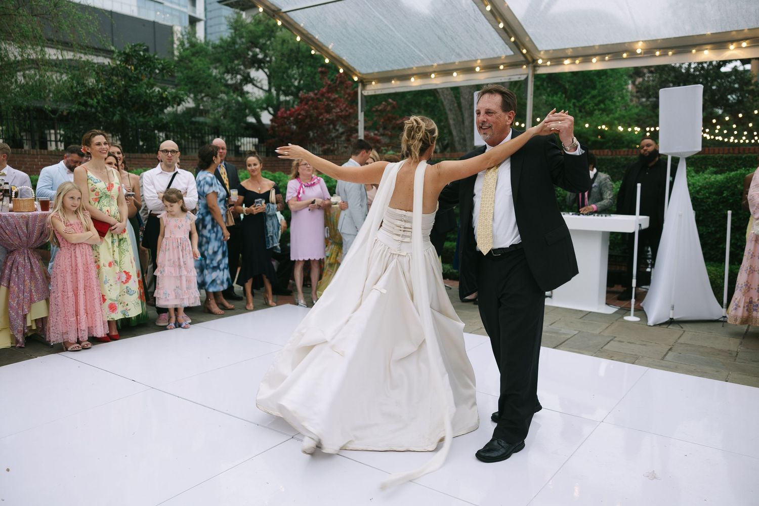 Wedding guests watch as the newlyweds dance under a white tent with string lights.
