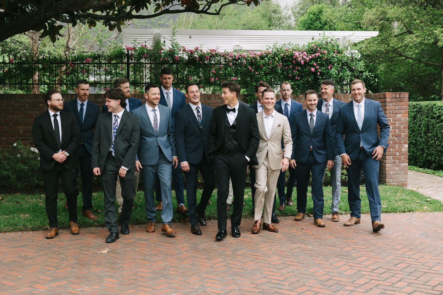 Groomsmen gather for casual group photos on outdoor garden path.