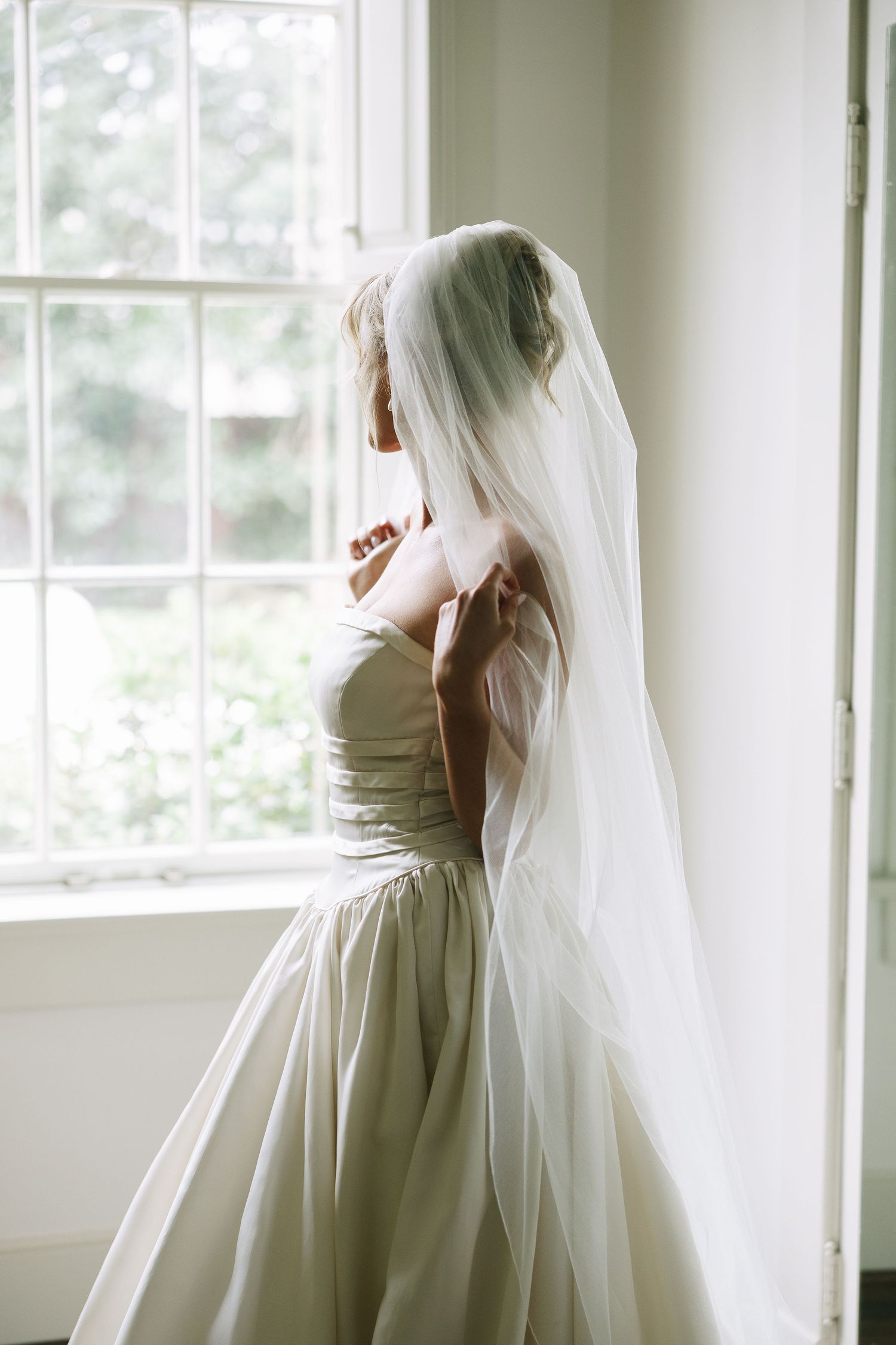 Ethereal bridal portraits with flowing veil in sunlit room with large windows.