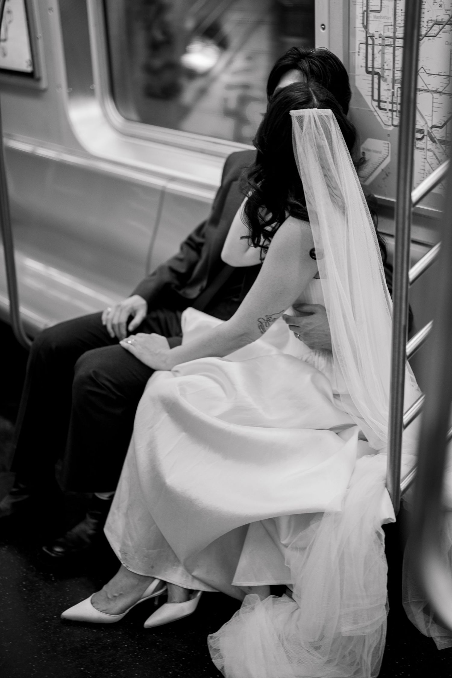 Couple in wedding attire sitting together on subway train with flowing white veil.