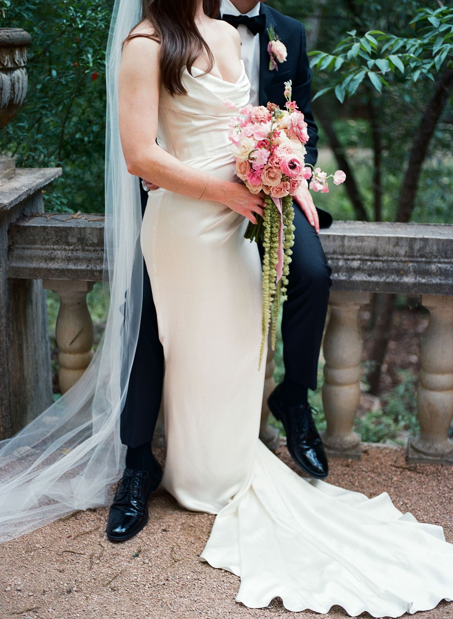 Close-up details of bride's flowing white dress and pink bouquet in garden setting.
