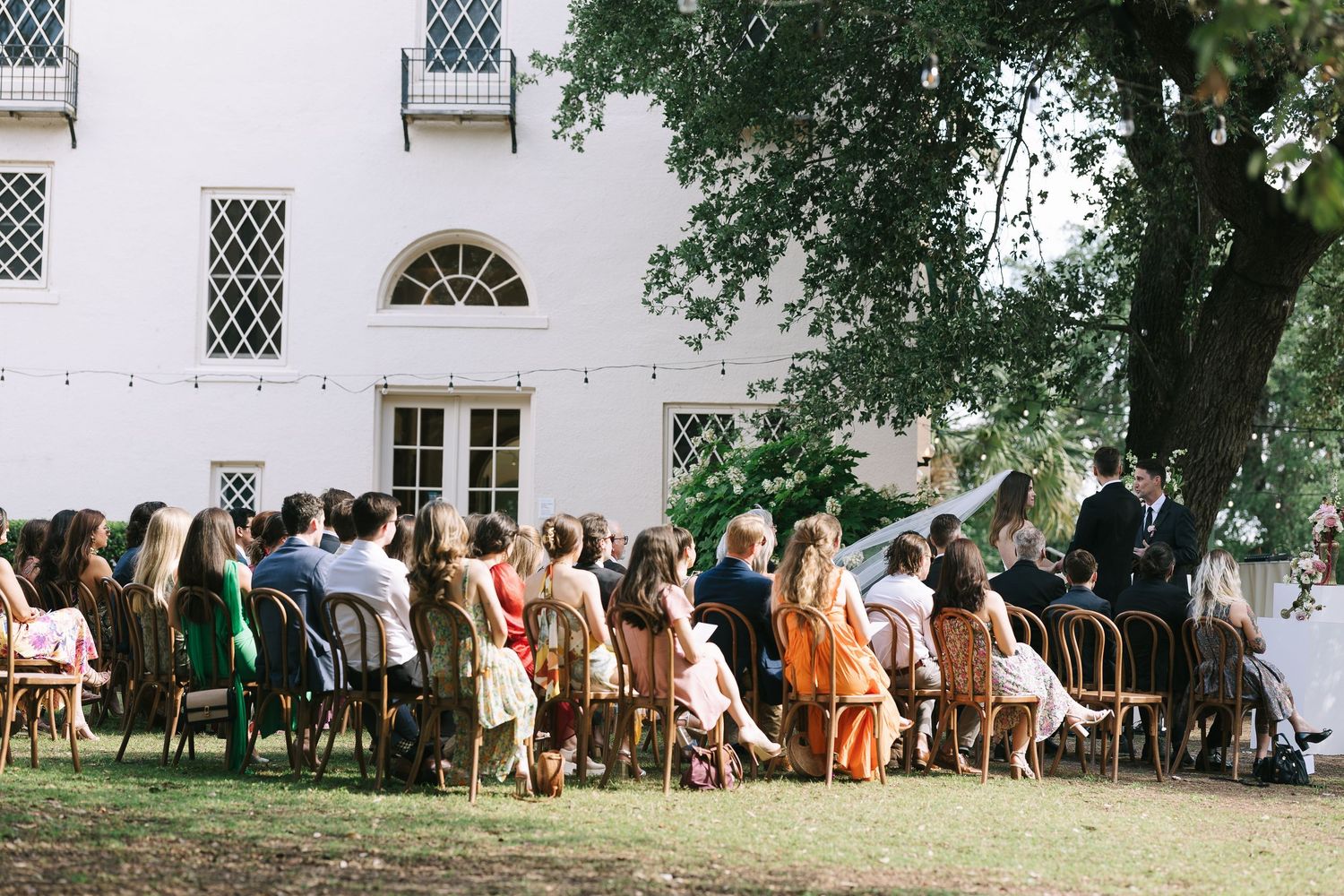 Long distance view of wedding ceremony setup with white building in background.