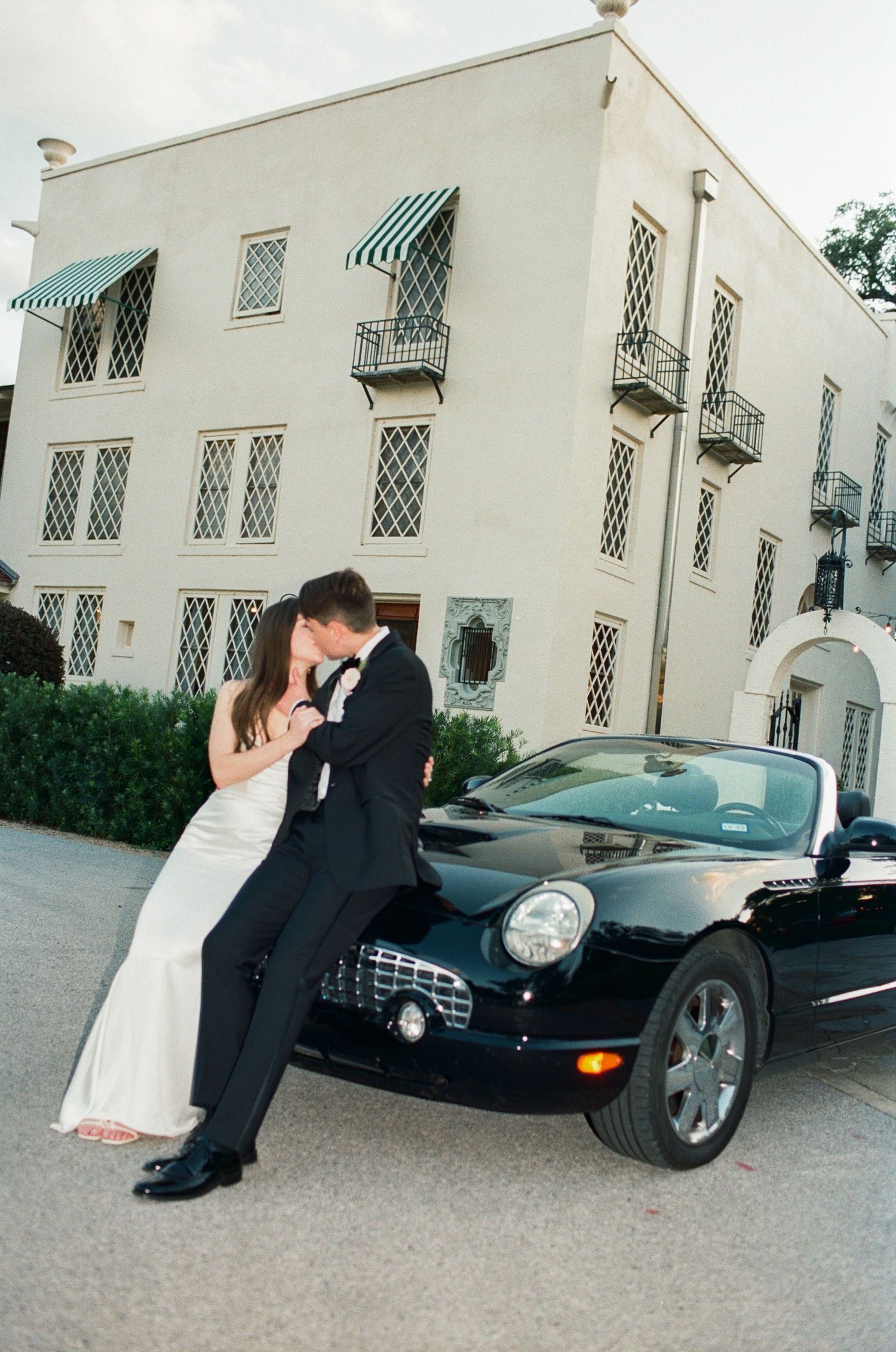 A romantic photoshoot featuring a couple posing with a sleek black sports car.