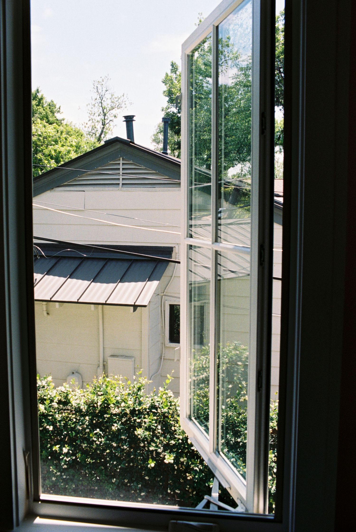 Sunlit view through large windows showing residential exterior and landscaping.