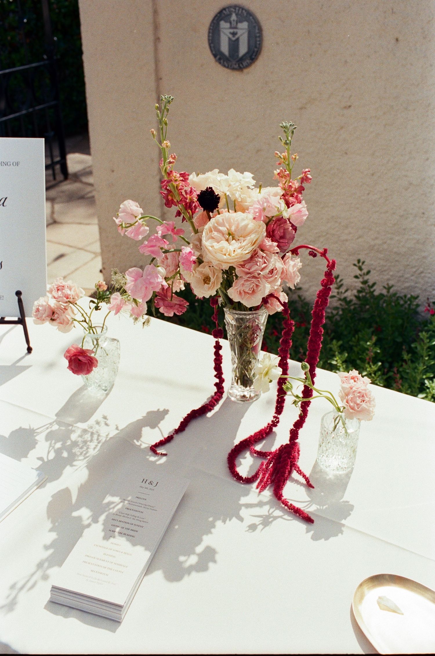 Elegant table setting with pink floral arrangements and menu cards casting shadows.