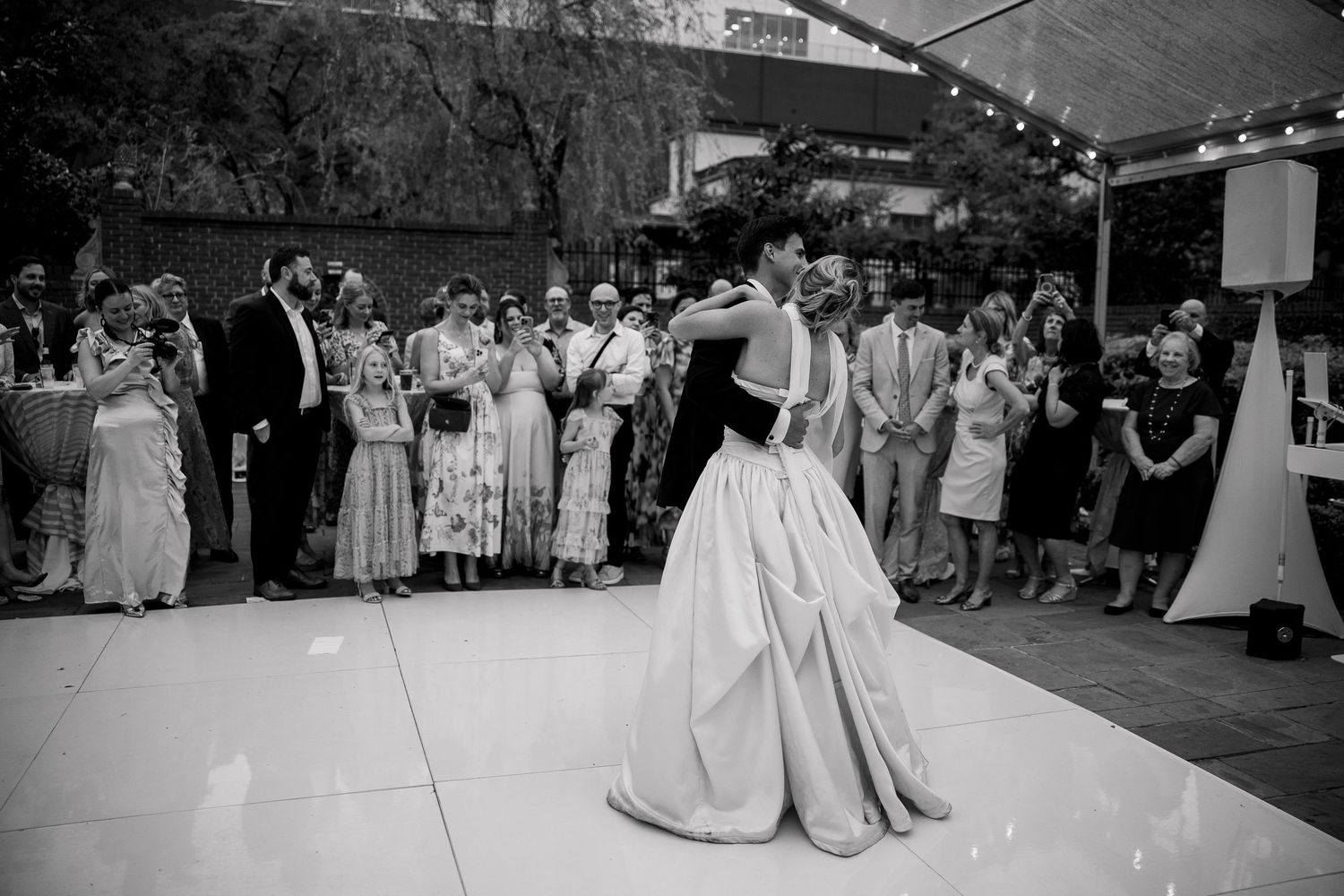 Wedding celebration on an outdoor dance floor with guests watching from the sides.